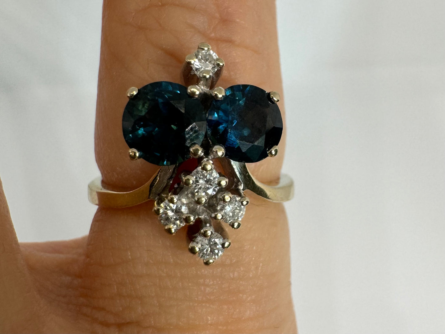 14K gold ring set with two deep blue oval Sapphires accented by clusters of brilliant white Diamonds.