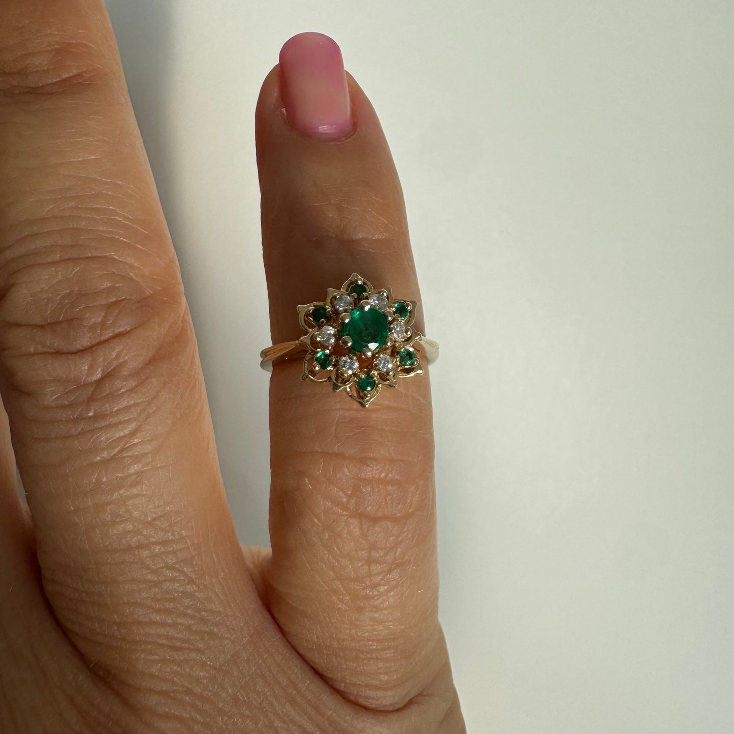טבעת זהב 14 קראט בעיצוב פרח משובצת אבן אמרלד מרכזית, מוקפת יהלומים ואבני אמרלד נוספות