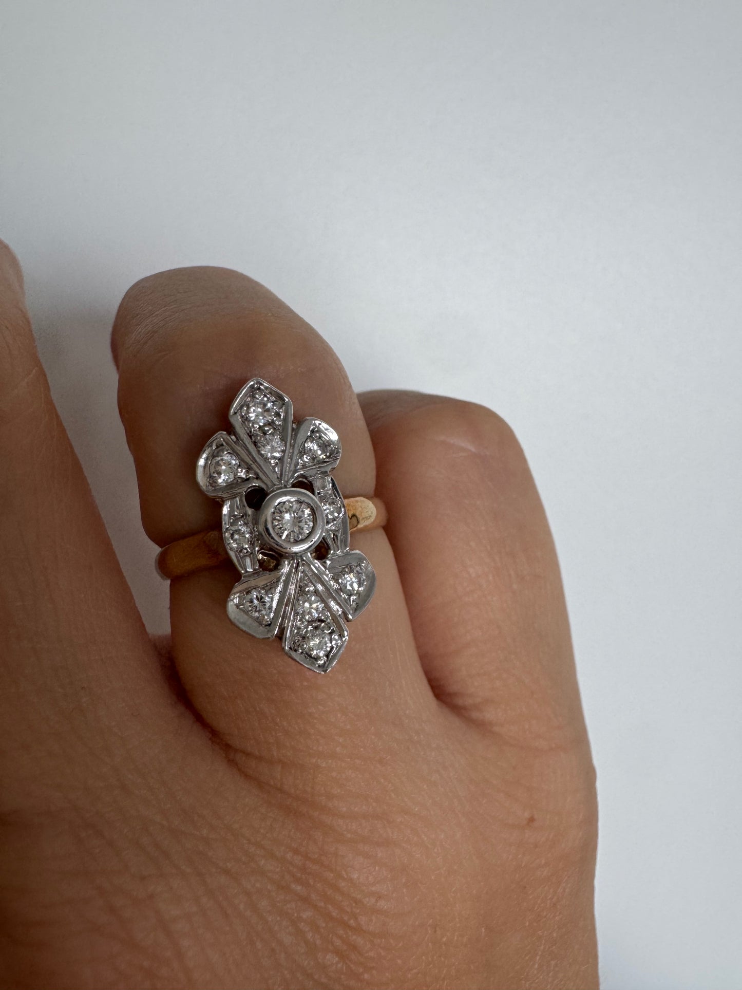 טבעת זהב לבן 14 קראט, בעיצוב אלגנטי ועדין, משובצת יהלום מרכזי עגול וסביבו יהלומים נוצצים נוספים.