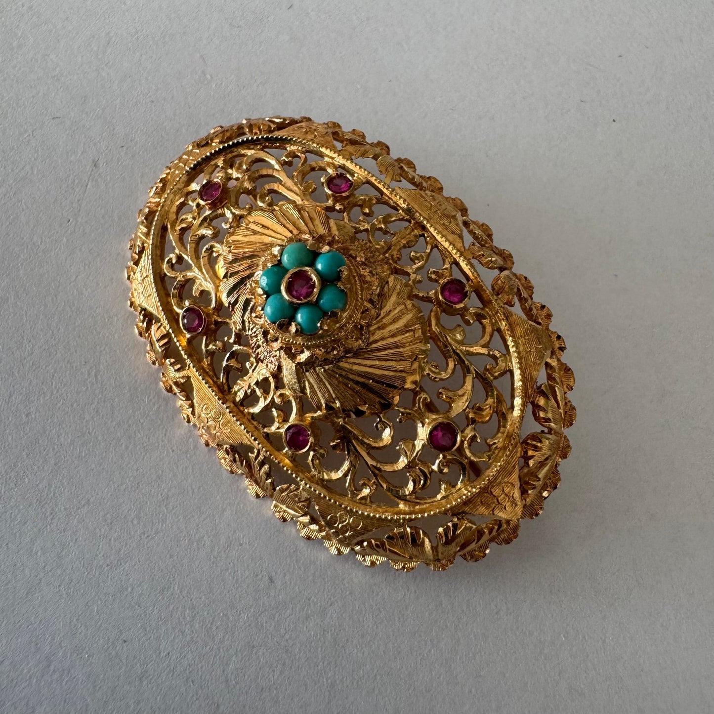 18K gold filigree brooch featuring intricate openwork detailing, accented with Ruby & Turquoise arranged in a floral centerpiece