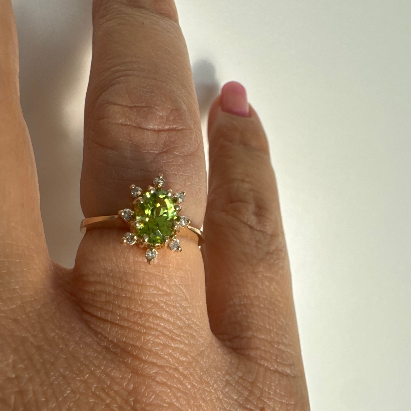 טבעת זהב 14 קראט משובצת אבן פרידוט ירוקה בחיתוך אובלי, מוקפת יהלומים היוצרים הילה עדינה מסביבה.