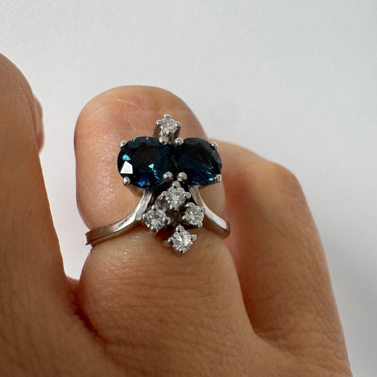 14K gold ring set with two deep blue oval Sapphires accented by clusters of brilliant white Diamonds.