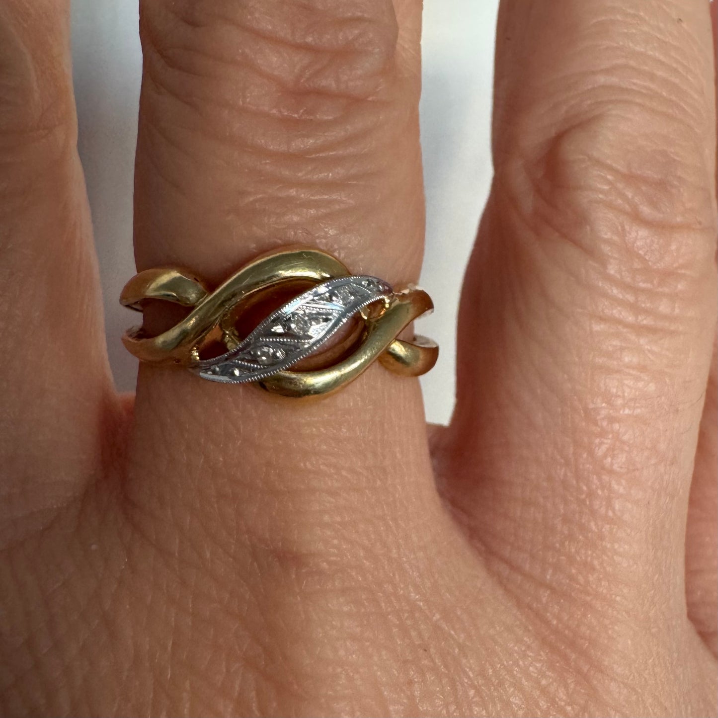 טבעת זהב צהוב 18 קראט בעיצוב קשר קלאסי, בשילוב אלמנט מרכזי מזהב לבן משובץ יהלומים עדינים.