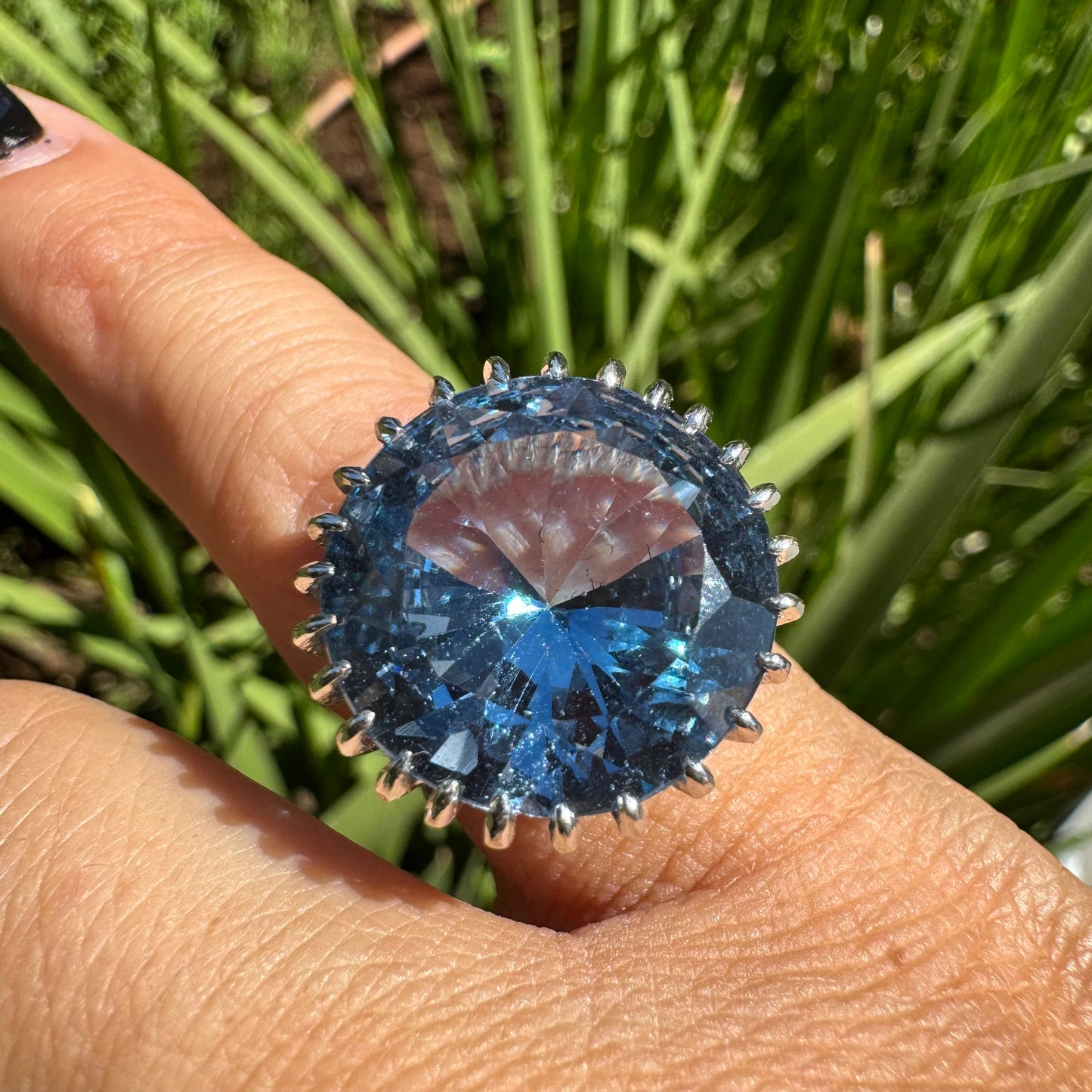 טבעת זהב לבן 14 קראט משובצת אבן טופז בצבע כחול, בולטת, בחיתוך עגול, משובצת במסגרת שיניים גבוהה ליצירת מראה מרשים ותופס עין