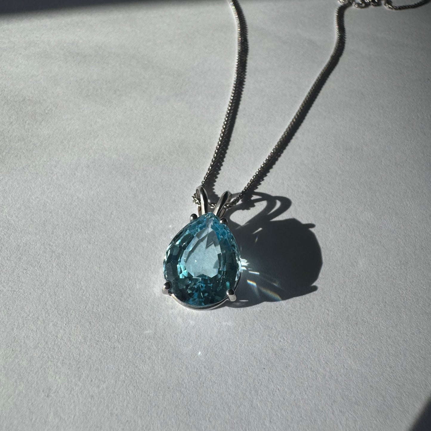 תליון זהב לבן 14 קראט המשובץ אבן טופז כחולה בחיתוך טיפה.