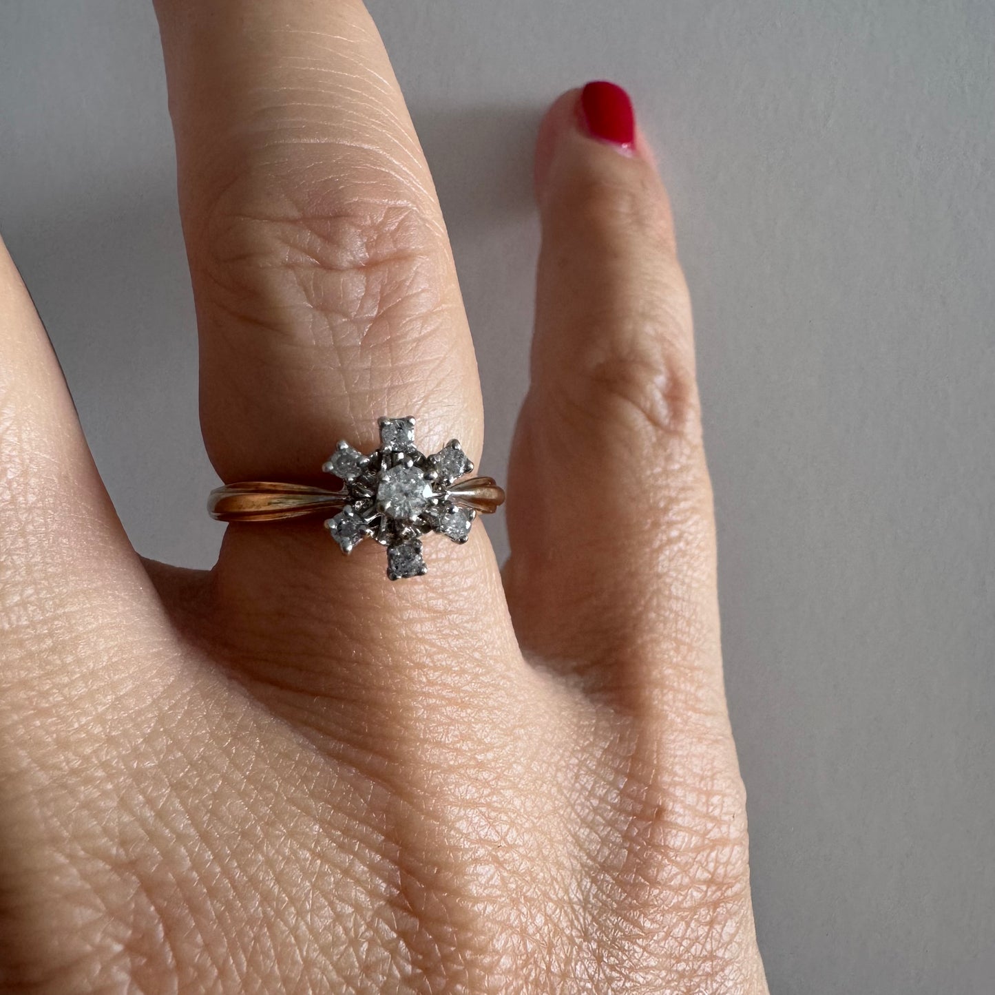 טבעת זהב 9 קראט משובצת יהלום מרכזי ויהלומים מסביב בעיצוב פרח קלאסי.