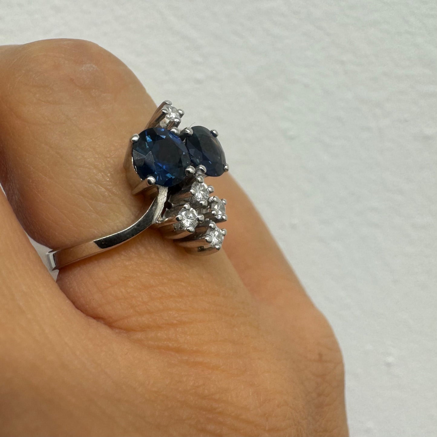 14K gold ring set with two deep blue oval Sapphires accented by clusters of brilliant white Diamonds.