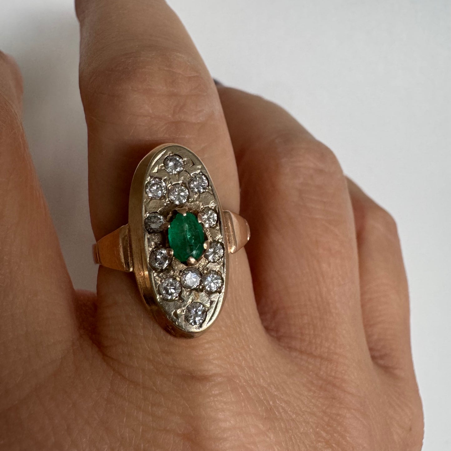 טבעת זהב 14 קראט בעיצוב אלגנטי ומאורך, משובצת אבן אמרלד מרכזית ויהלומים מסביב.