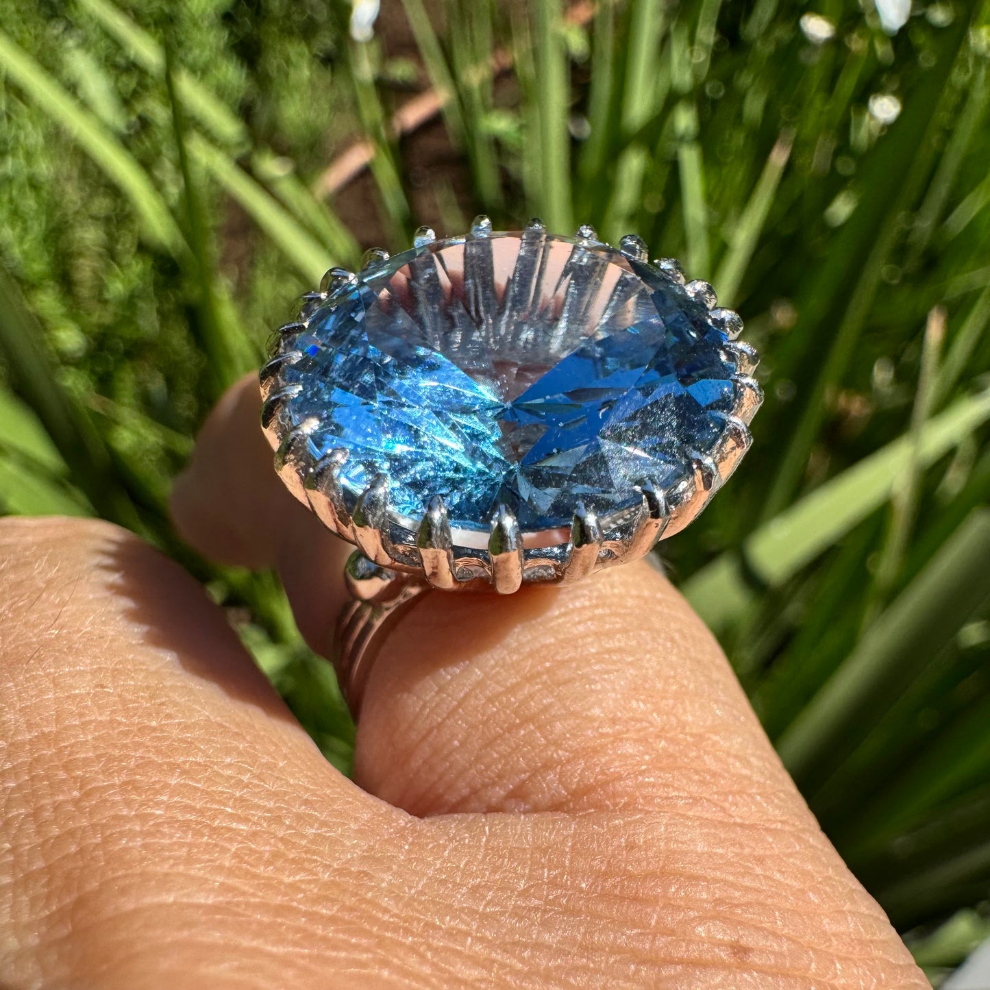 טבעת זהב לבן 14 קראט משובצת אבן טופז בצבע כחול, בולטת, בחיתוך עגול, משובצת במסגרת שיניים גבוהה ליצירת מראה מרשים ותופס עין