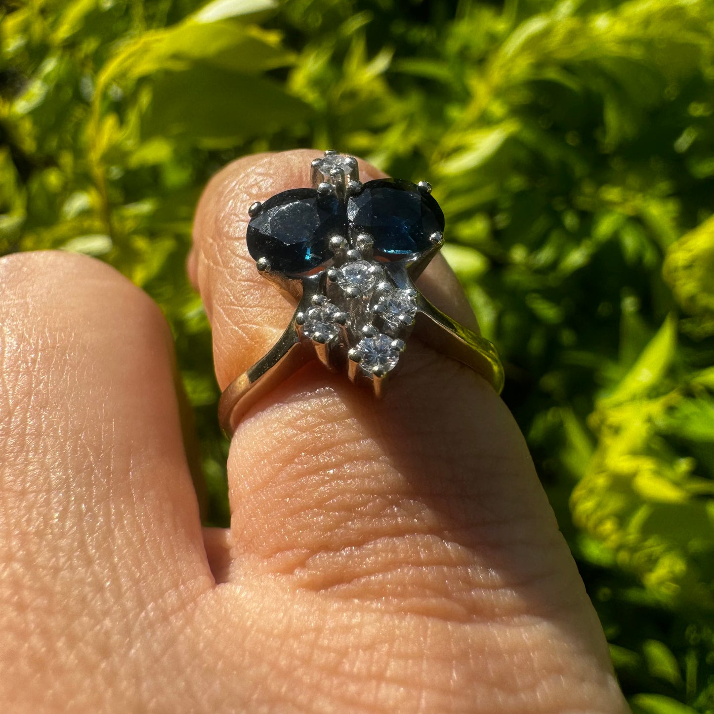 14K gold ring set with two deep blue oval Sapphires accented by clusters of brilliant white Diamonds.