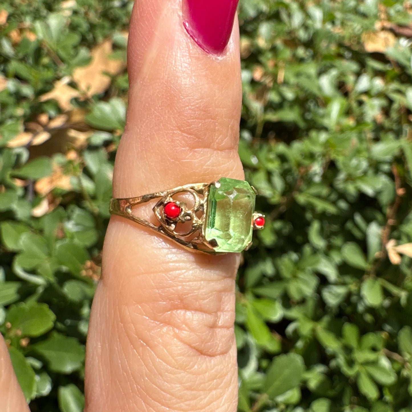 14K gold ring set with a vibrant emerald-cut Peridot at its center, flanked by two delicate red Coral accents