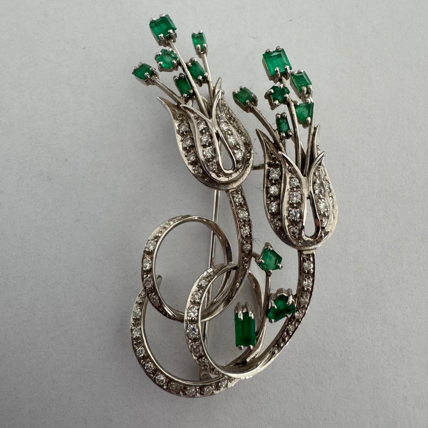 18K gold vintage brooch featuring an elegant floral design set with vibrant Emeralds and sparkling Diamonds.