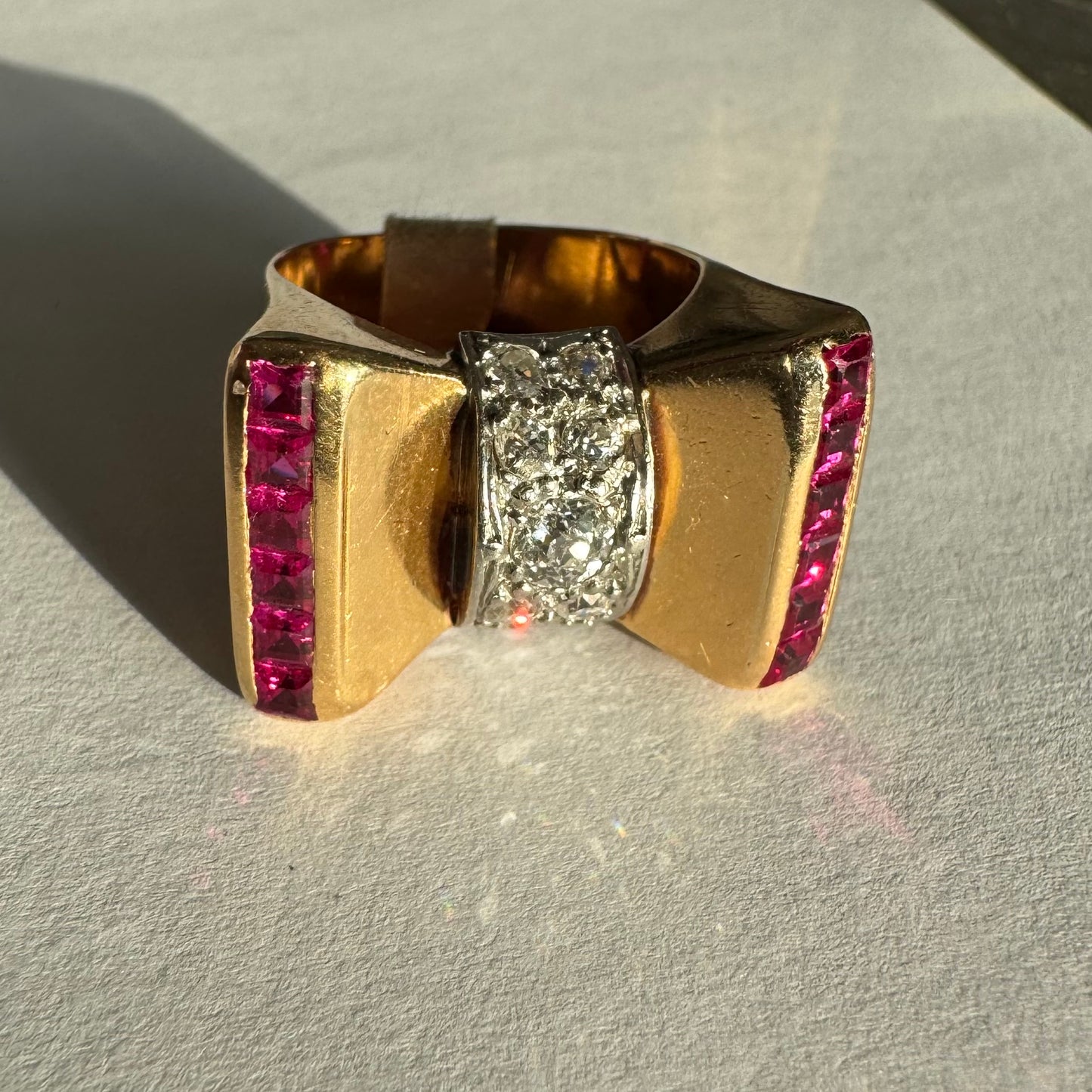 טבעת זהב 18 קראט בצורת פפיון, משובצת יהלומים במרכז ובאבני רובי בחיתוך מרובע בצדדים.