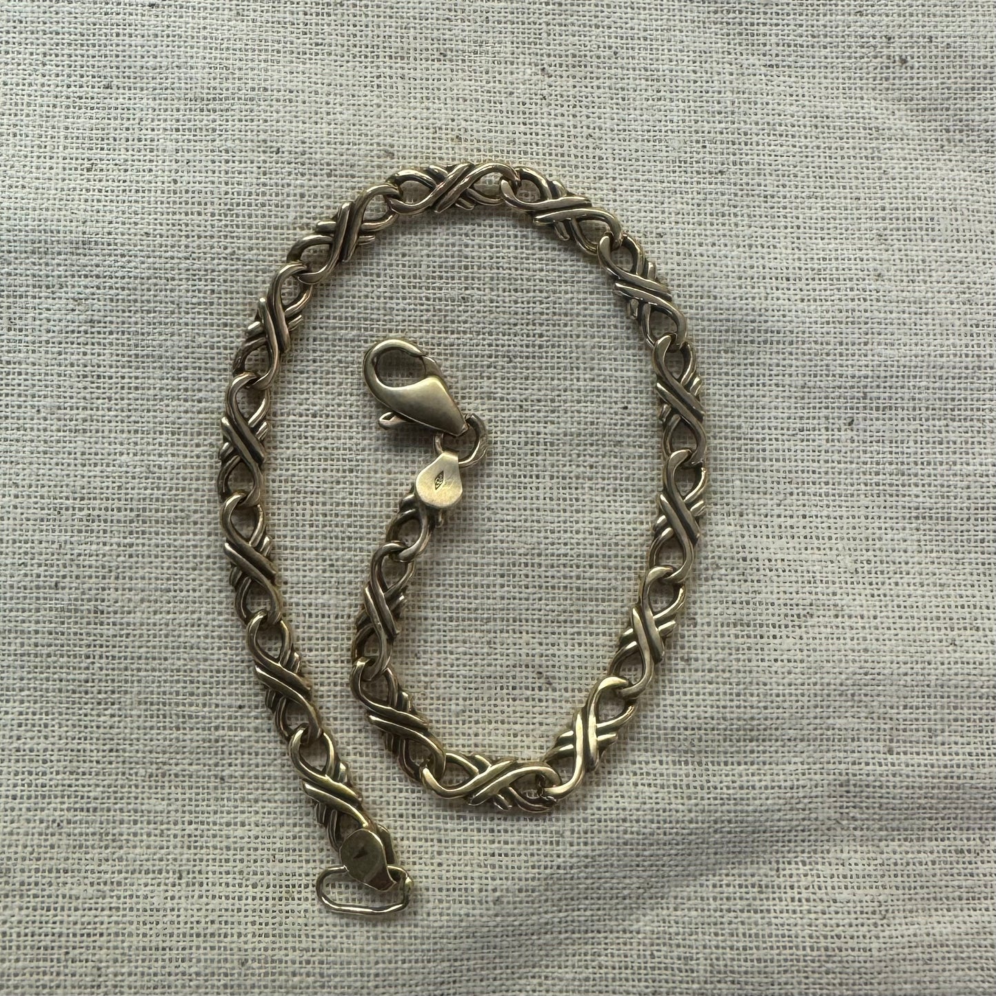 14K gold bracelet with an interwoven twisted link design and a lobster clasp closure.