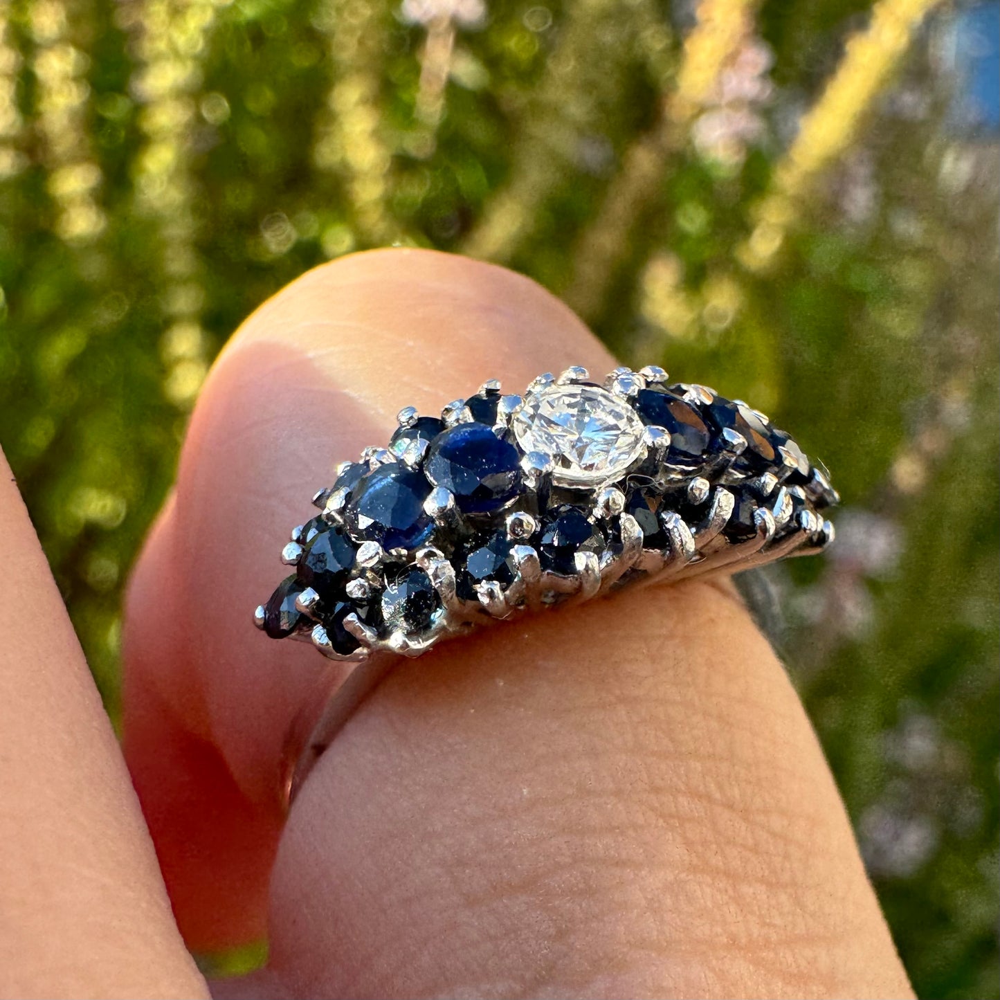 18K gold ring set with a brilliant-cut central Diamond, surrounded by a striking cluster of deep blue Sapphires.