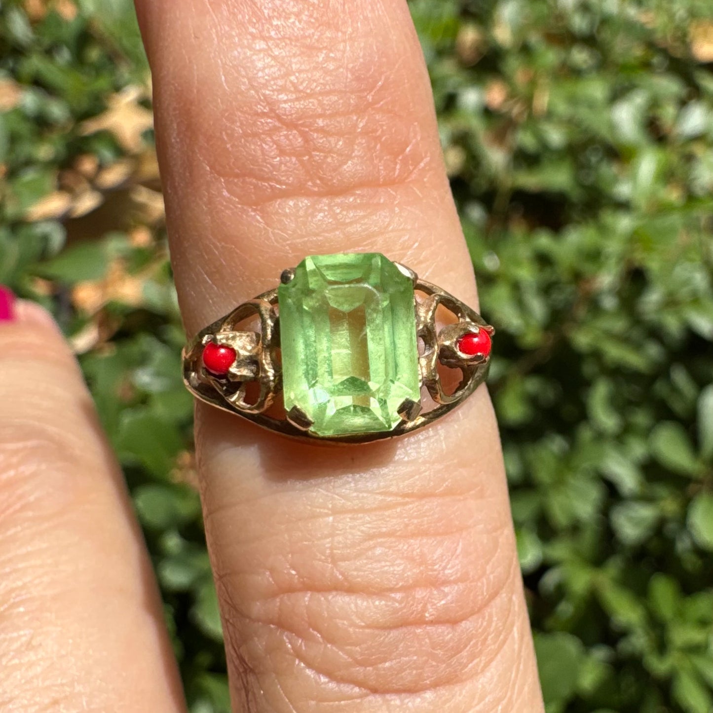 14K gold ring set with a vibrant emerald-cut Peridot at its center, flanked by two delicate red Coral accents