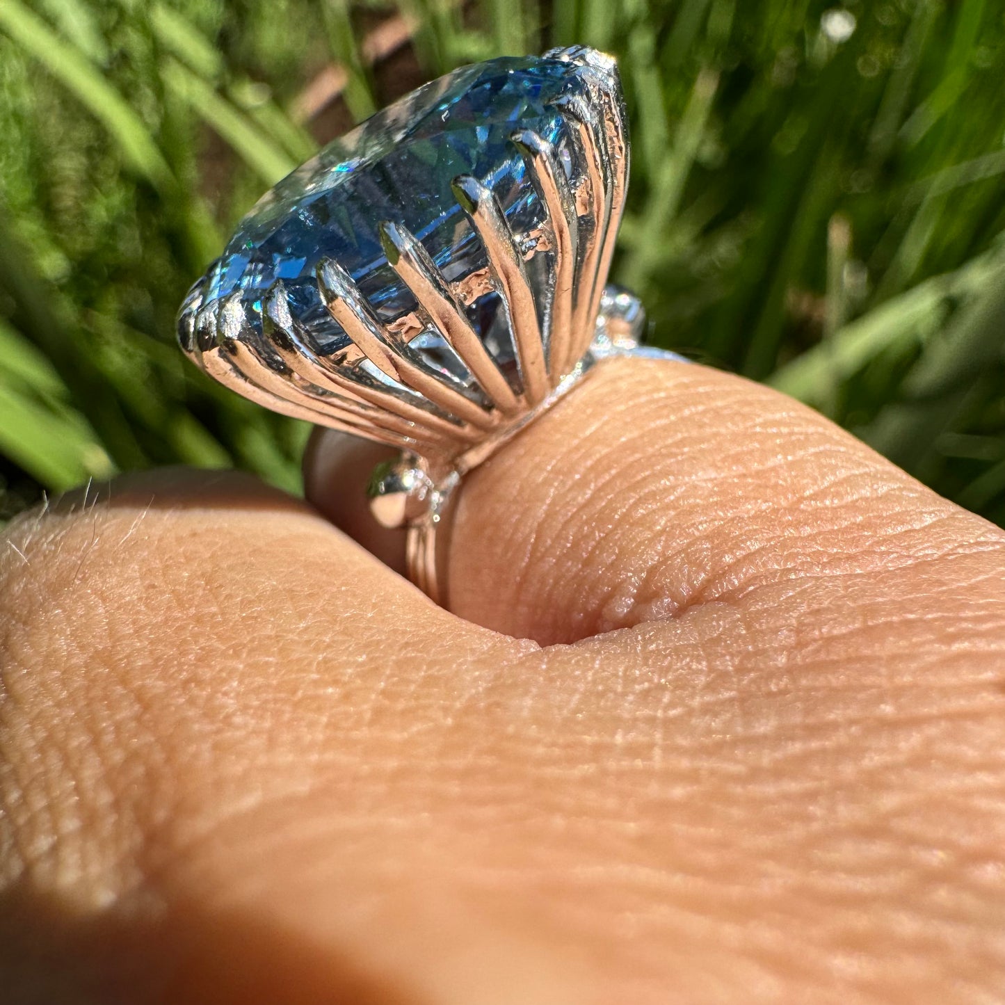 טבעת זהב לבן 14 קראט משובצת אבן טופז בצבע כחול, בולטת, בחיתוך עגול, משובצת במסגרת שיניים גבוהה ליצירת מראה מרשים ותופס עין