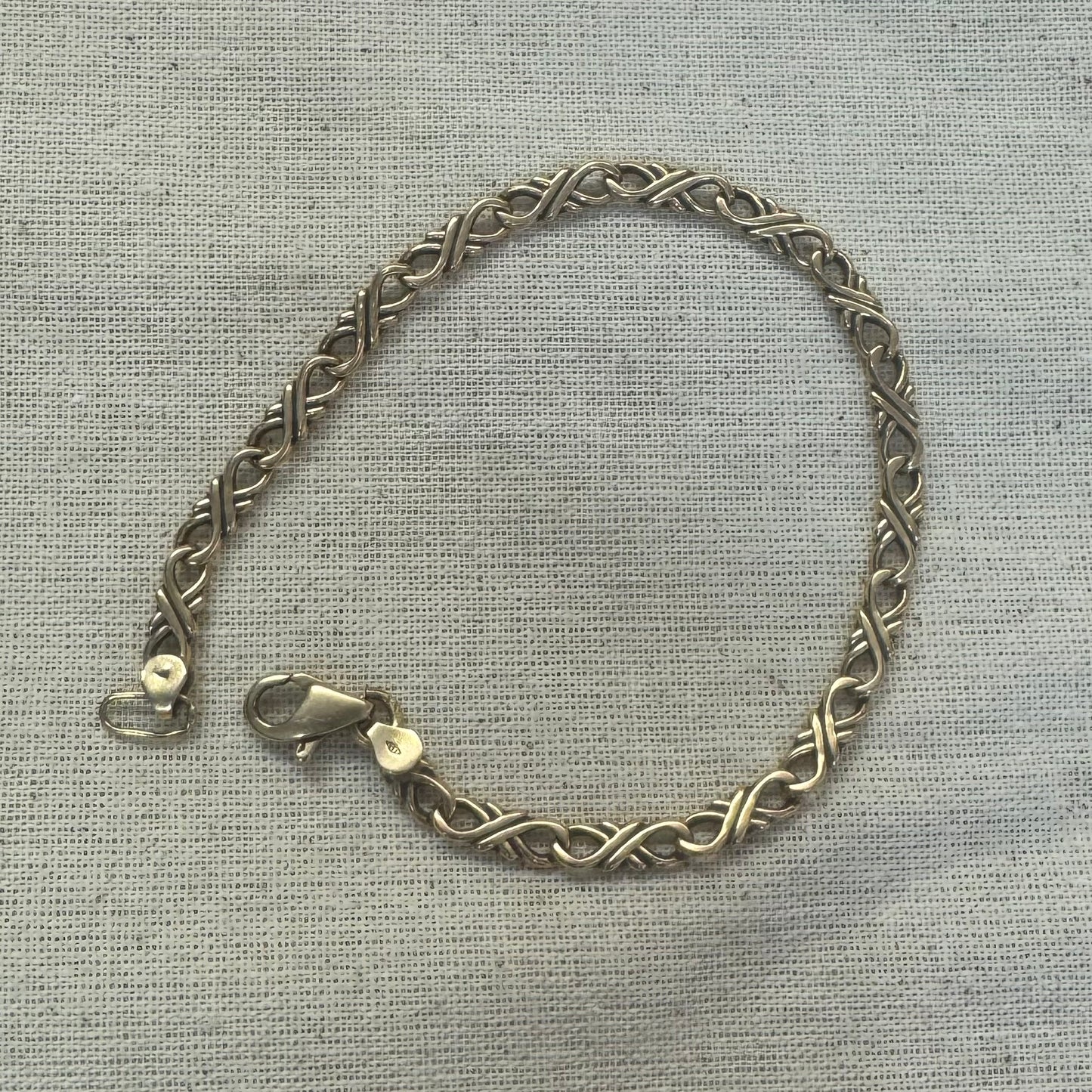 14K gold bracelet with an interwoven twisted link design and a lobster clasp closure.