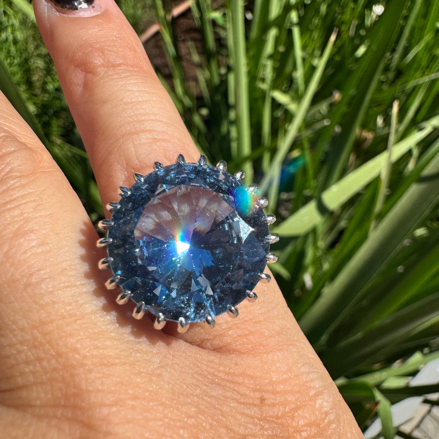 טבעת זהב לבן 14 קראט משובצת אבן טופז בצבע כחול, בולטת, בחיתוך עגול, משובצת במסגרת שיניים גבוהה ליצירת מראה מרשים ותופס עין