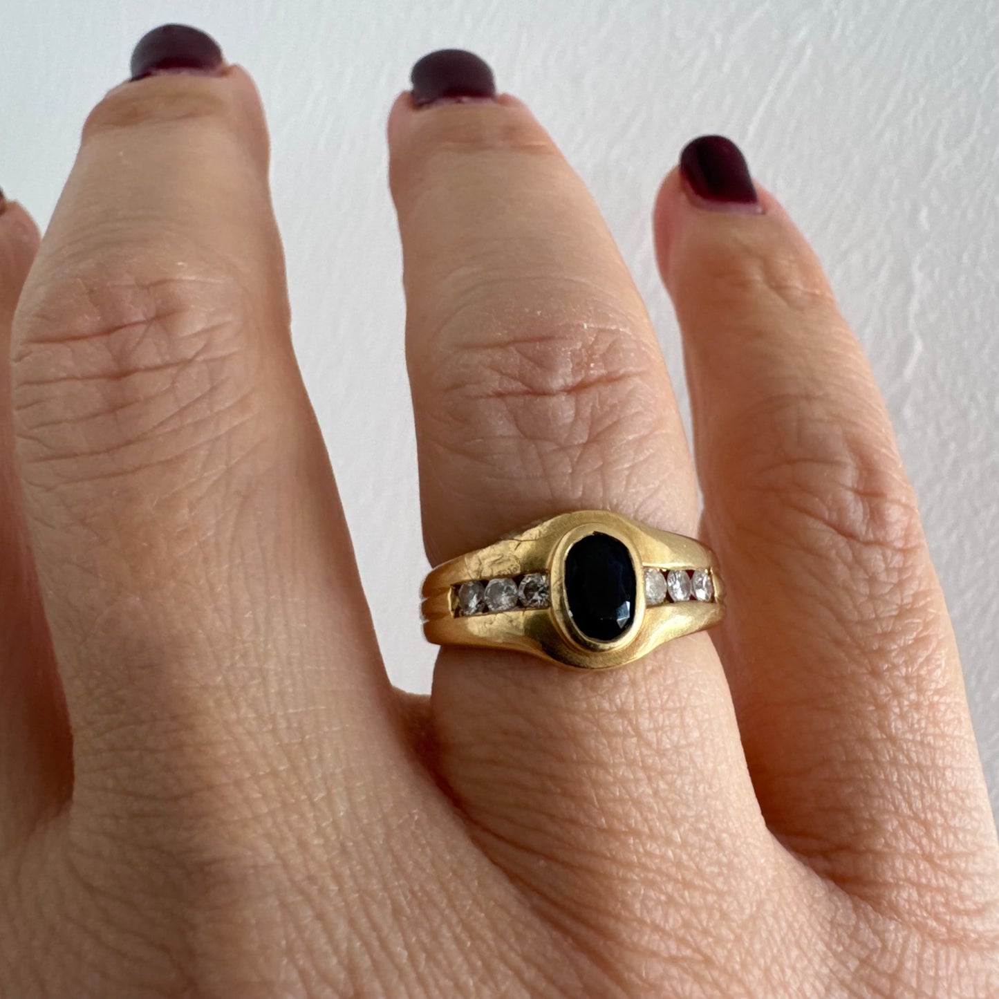 טבעת זהב צהוב 18 קראט משובצת אבן ספיר אובלית בגוון כחול עמוק, במסגרת חלקה ומודגשת, ומשני צדדיה שורת יהלומים משובצים בתעלה.