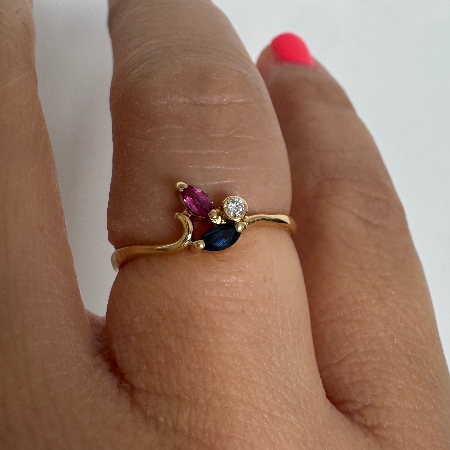 Delicate 18K gold ring set with pink and blue Sapphires alongside a sparkling center stone.