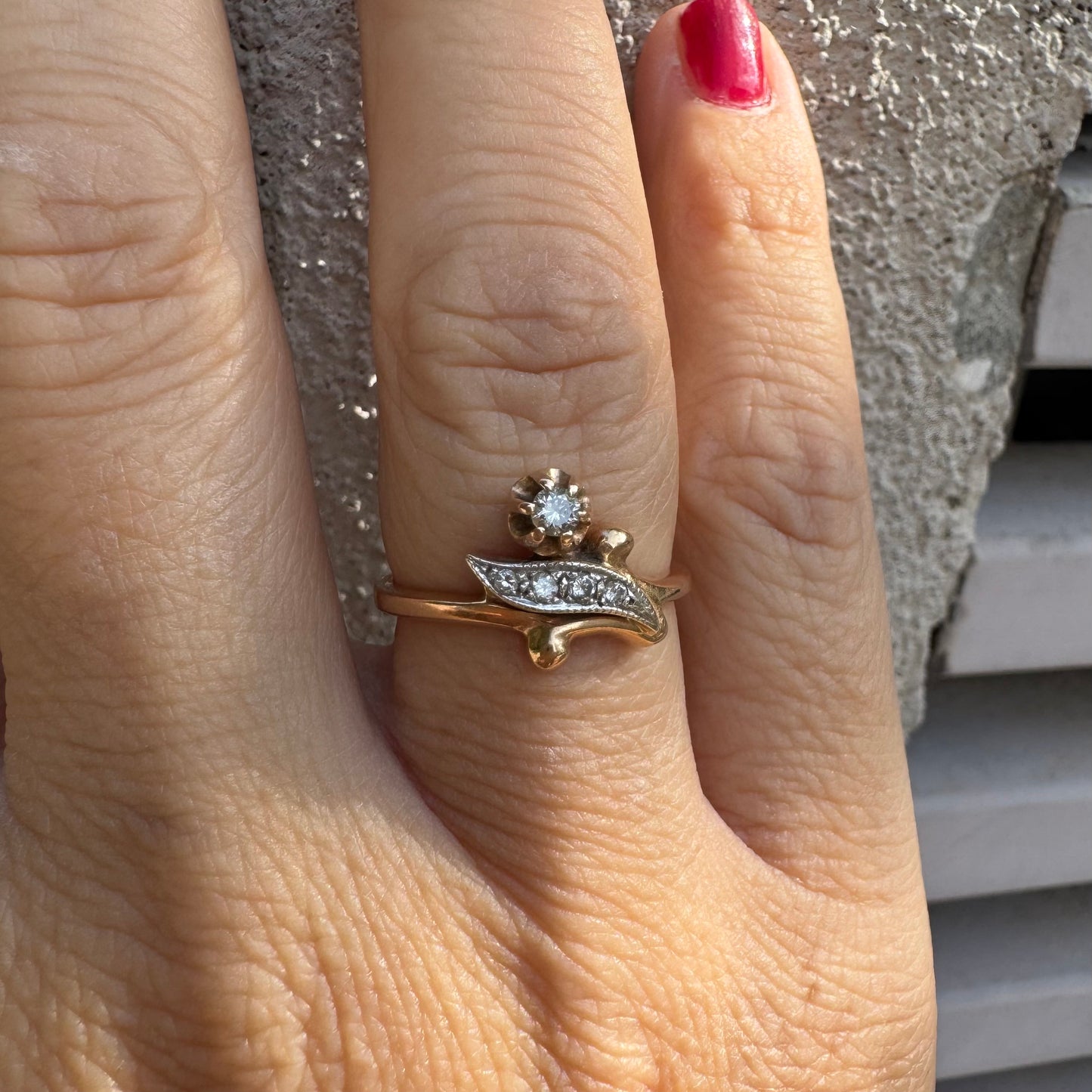 טבעת זהב אדום 14 קראט, עם שיבוץ בצורת פרח קטן ובו יהלום נוצץ לצד אלמנט מעוגל בצורת עלה משובץ יהלומים.