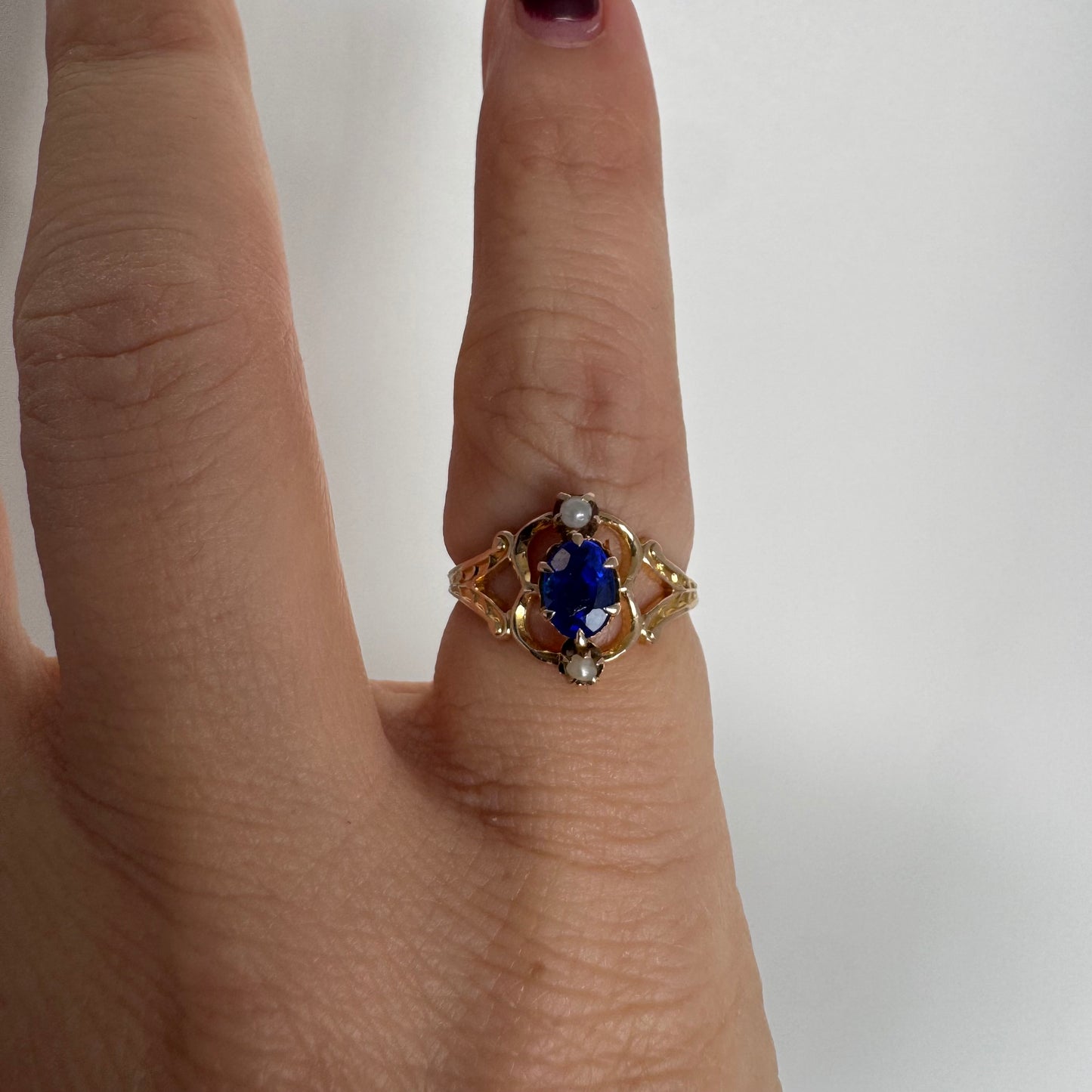 טבעת זהב צהוב 10 קראט משובצת אבן ספיר אובלית בגוון כחול עמוק ועשיר, ולצידה פנינים קטנות עדינות מעל ומתחת לאבן.