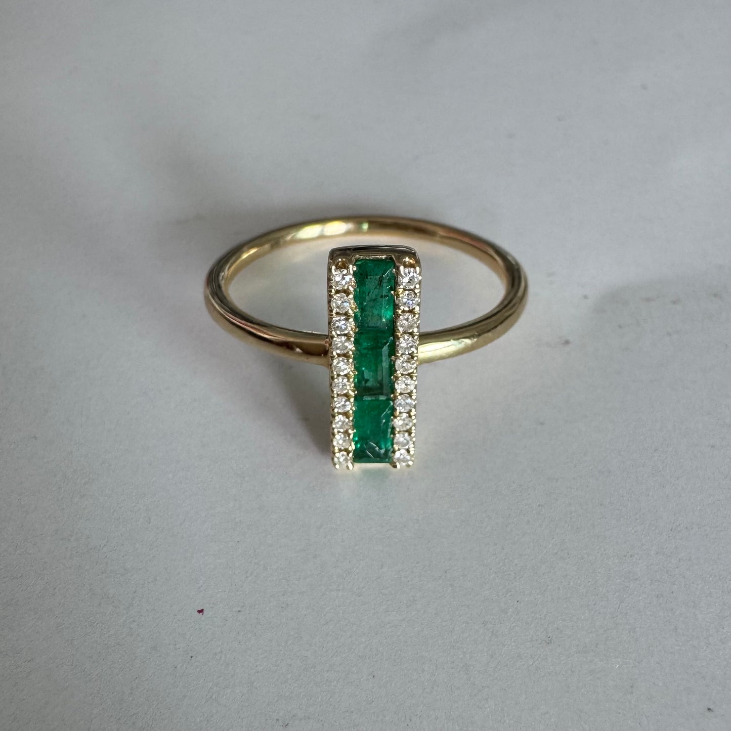 טבעת זהב 14 קראט משובצת אבני אמרלד בחיתוך באגט, מוקפות בשתי שורות של יהלומים נוצצים .