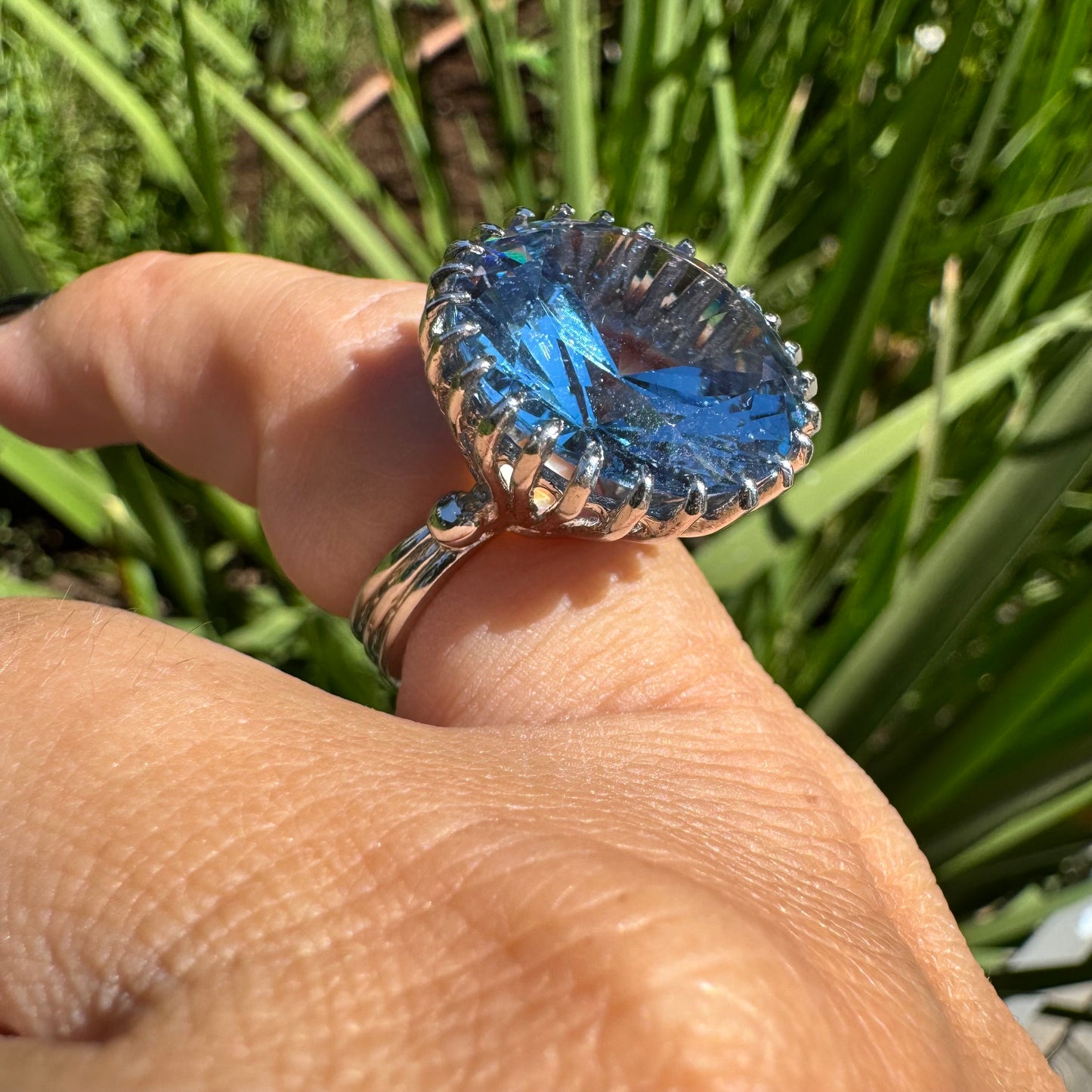 טבעת זהב לבן 14 קראט משובצת אבן טופז בצבע כחול, בולטת, בחיתוך עגול, משובצת במסגרת שיניים גבוהה ליצירת מראה מרשים ותופס עין