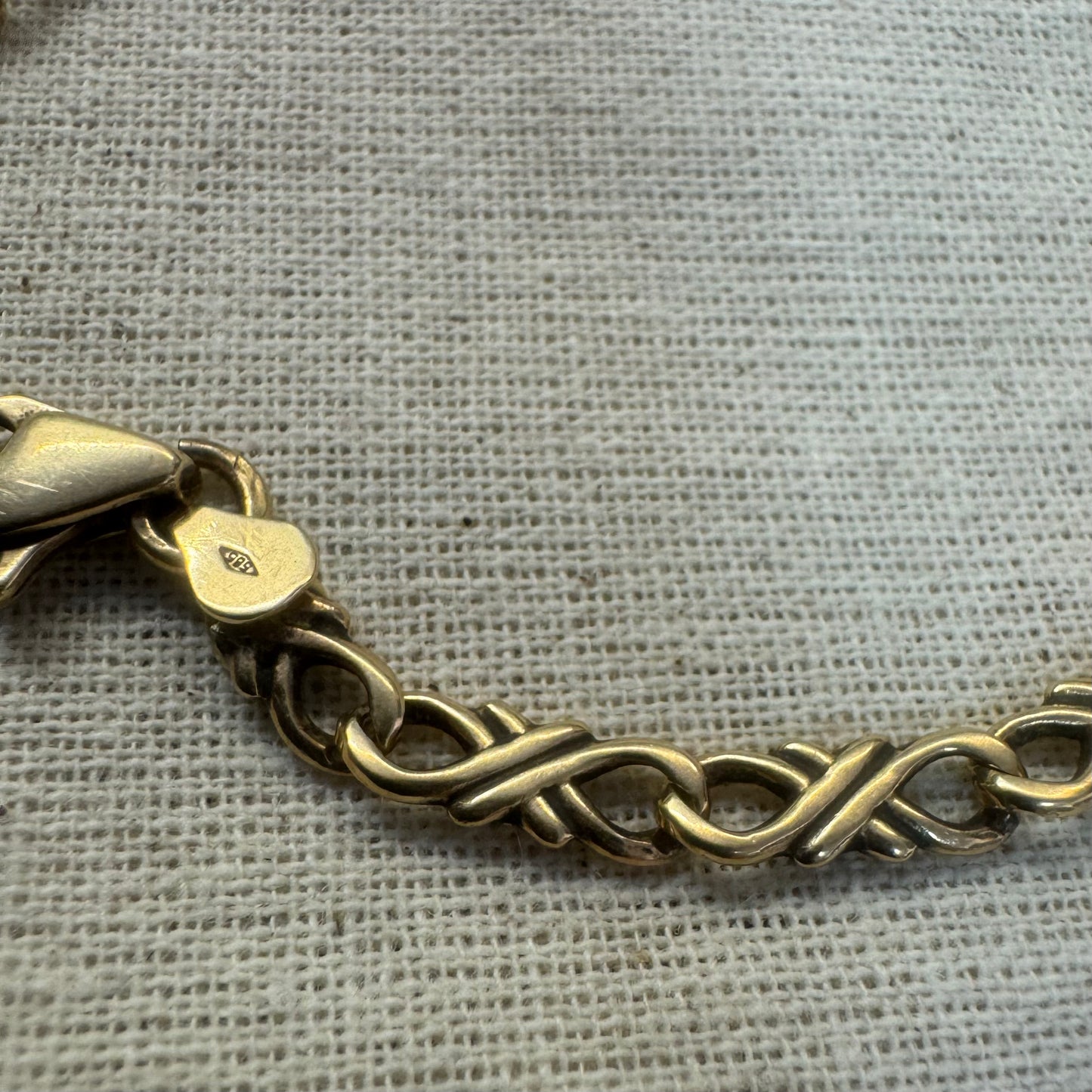 14K gold bracelet with an interwoven twisted link design and a lobster clasp closure.