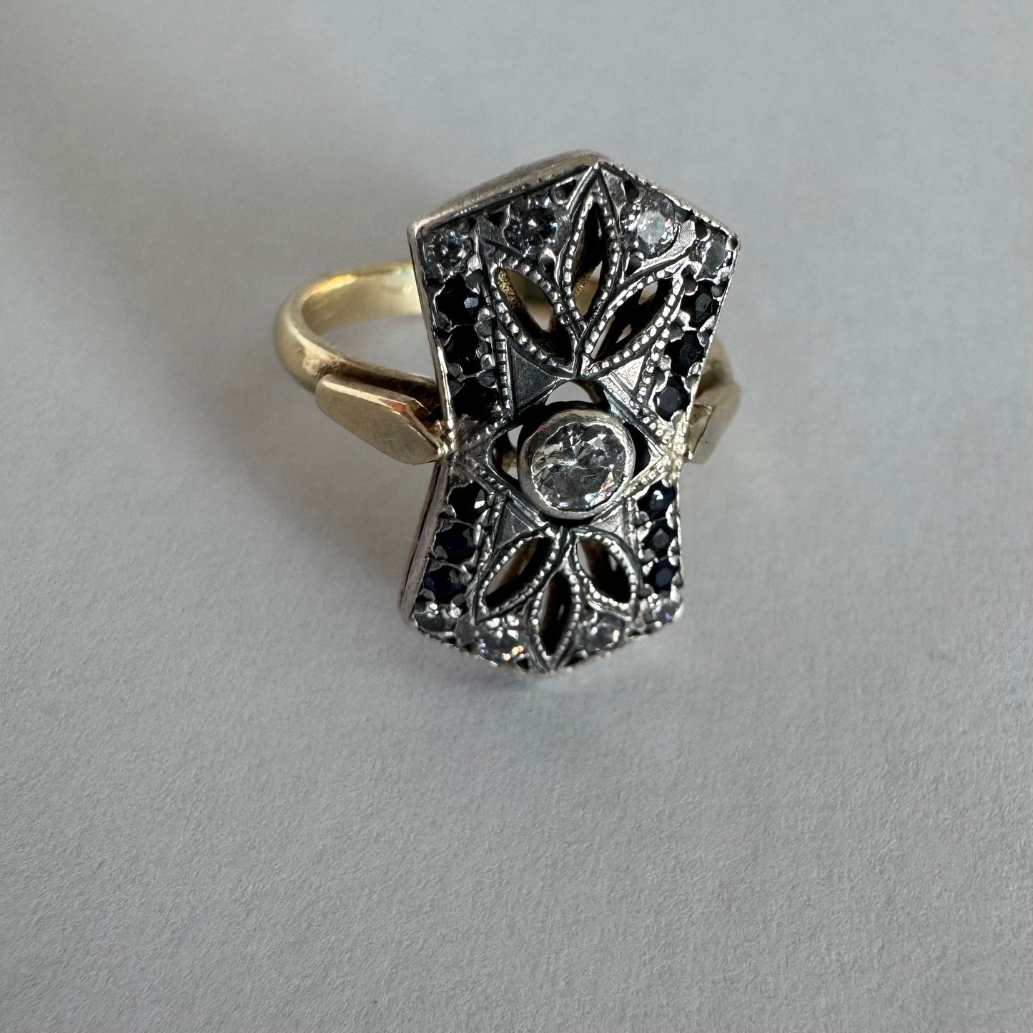 14K gold Art Deco ring set with a central Diamond, framed by deep blue Sapphires and accent Diamonds.