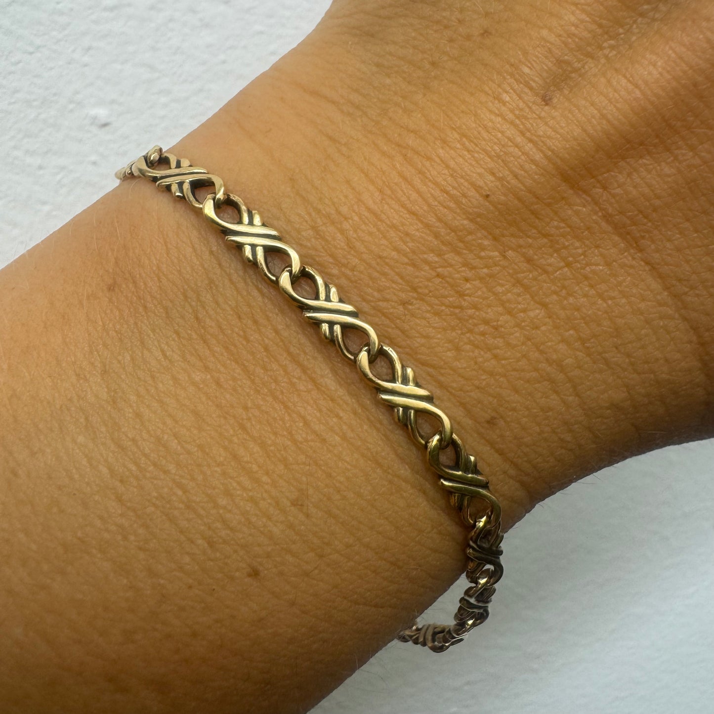 14K gold bracelet with an interwoven twisted link design and a lobster clasp closure.