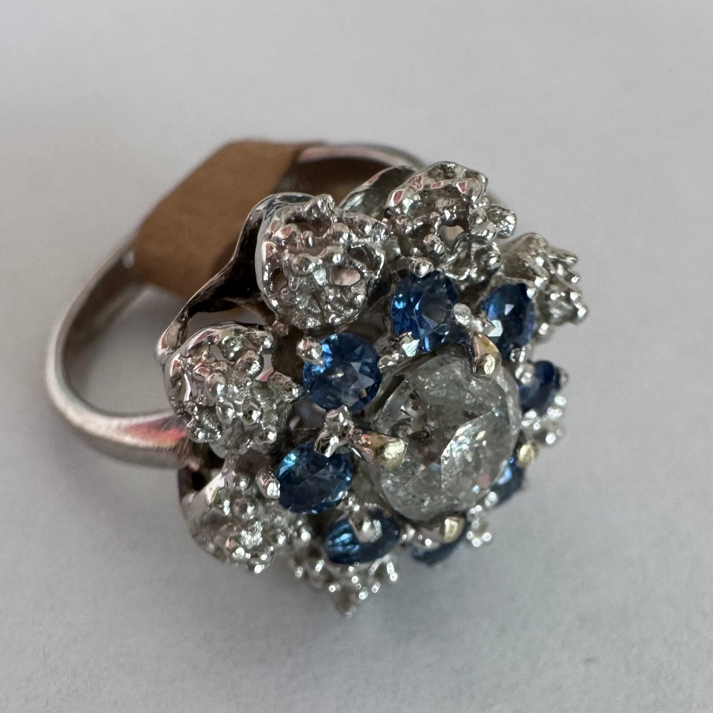 18K gold ring featuring a large round Diamond at the center, surrounded by a floral halo of purple -blue Tanzanite and & Diamonds.