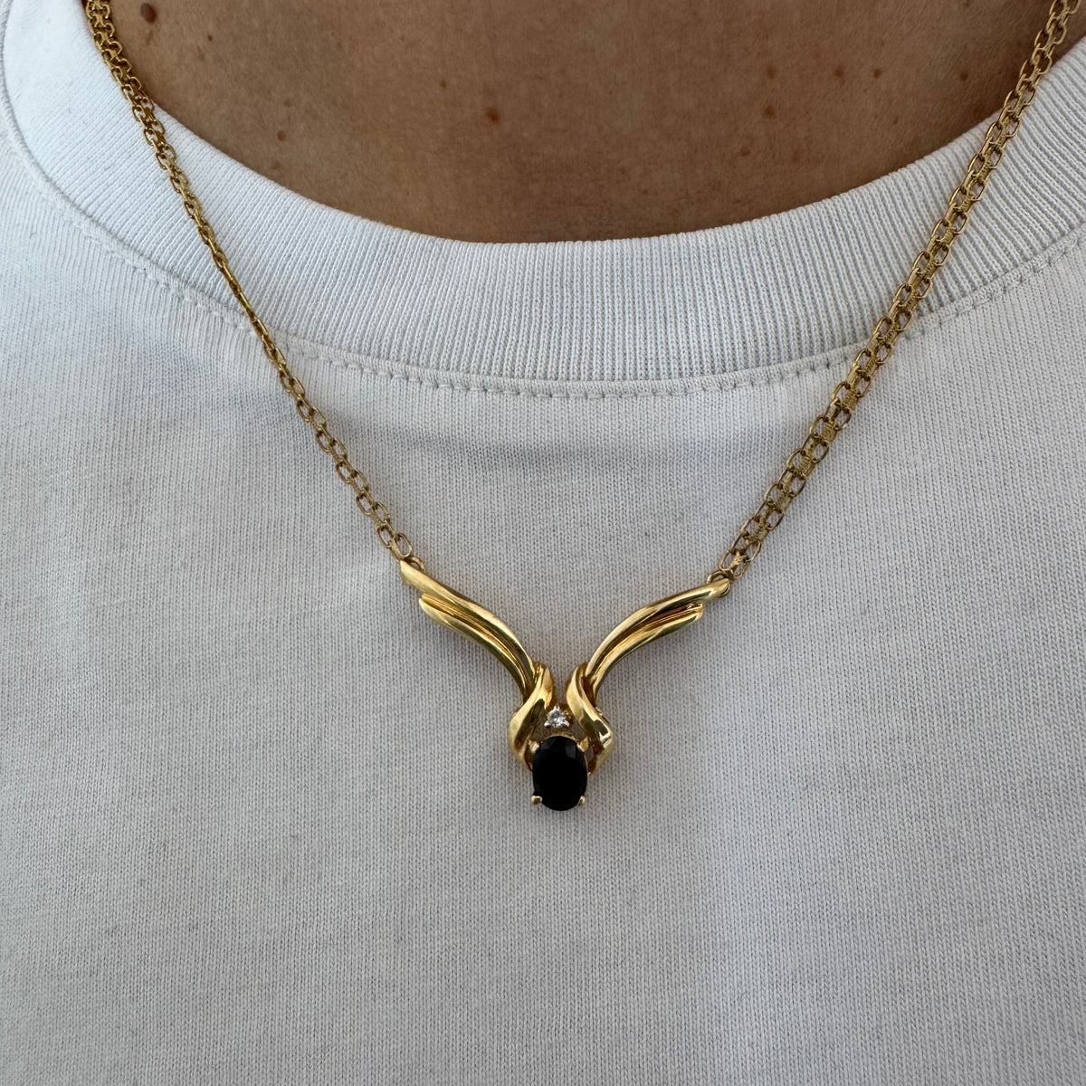 14K gold necklace featuring a flowing pendant design, set with a dark blue center Sapphire and a small Diamond above.