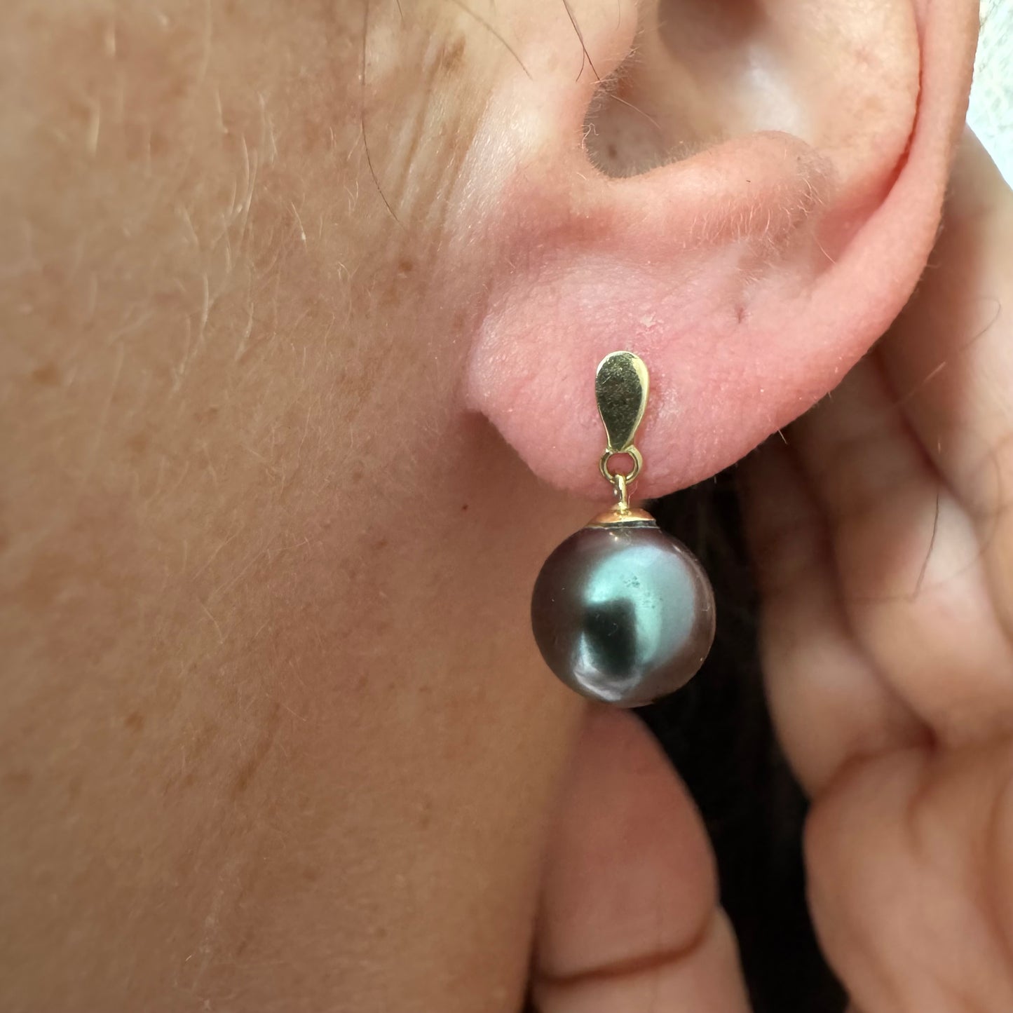 עגילי זהב צהוב 14 קראט משובצים פנינים עגולות בגוון כהה עם ברק עמוק ומשתנה.