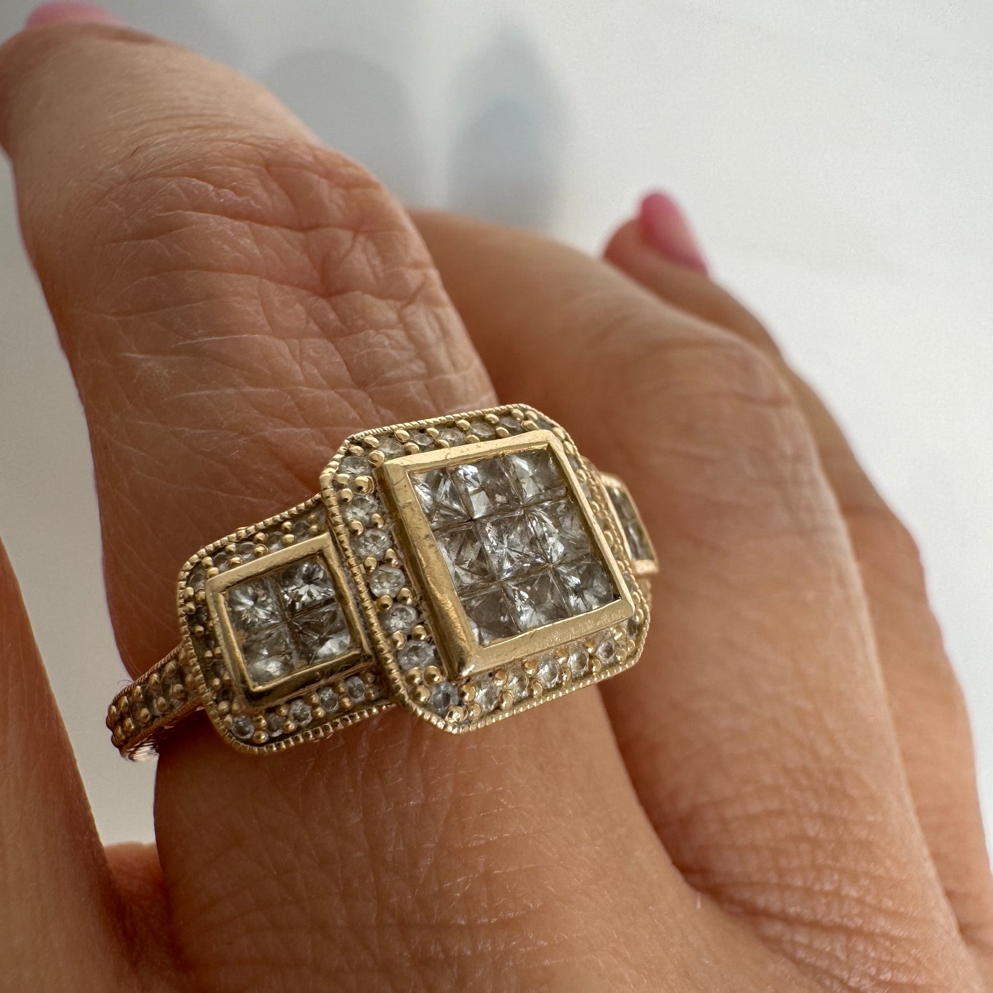 טבעת זהב צהוב 14 קראט משובצת יהלומים בחיתוך פרינסס במרכז, מוקפת הילה של יהלומים צדדיים.