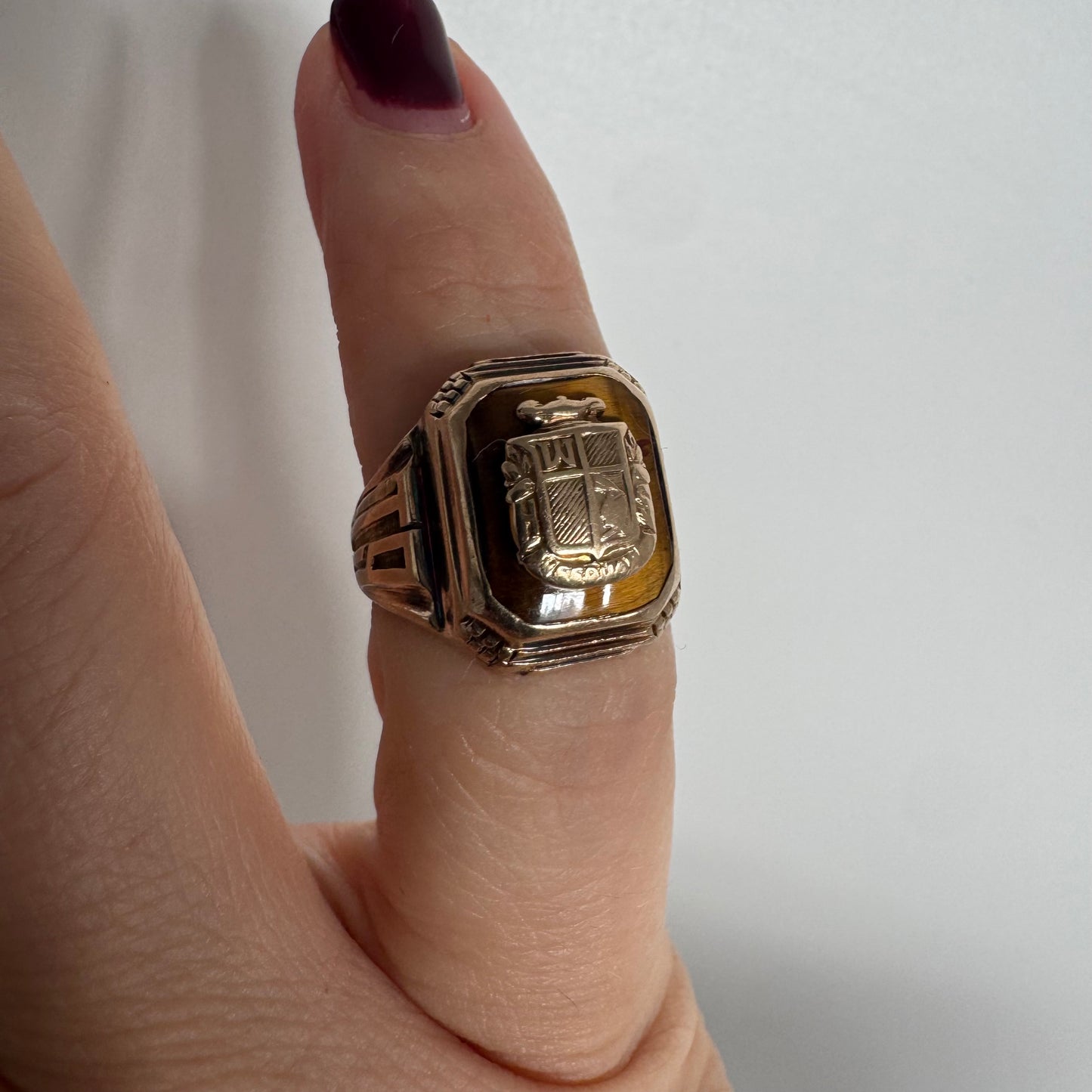 טבעת חותם זהב צהוב 10 קראט עם אבן בגוון חום-דבש ועיטור סמל מובלט במרכז.