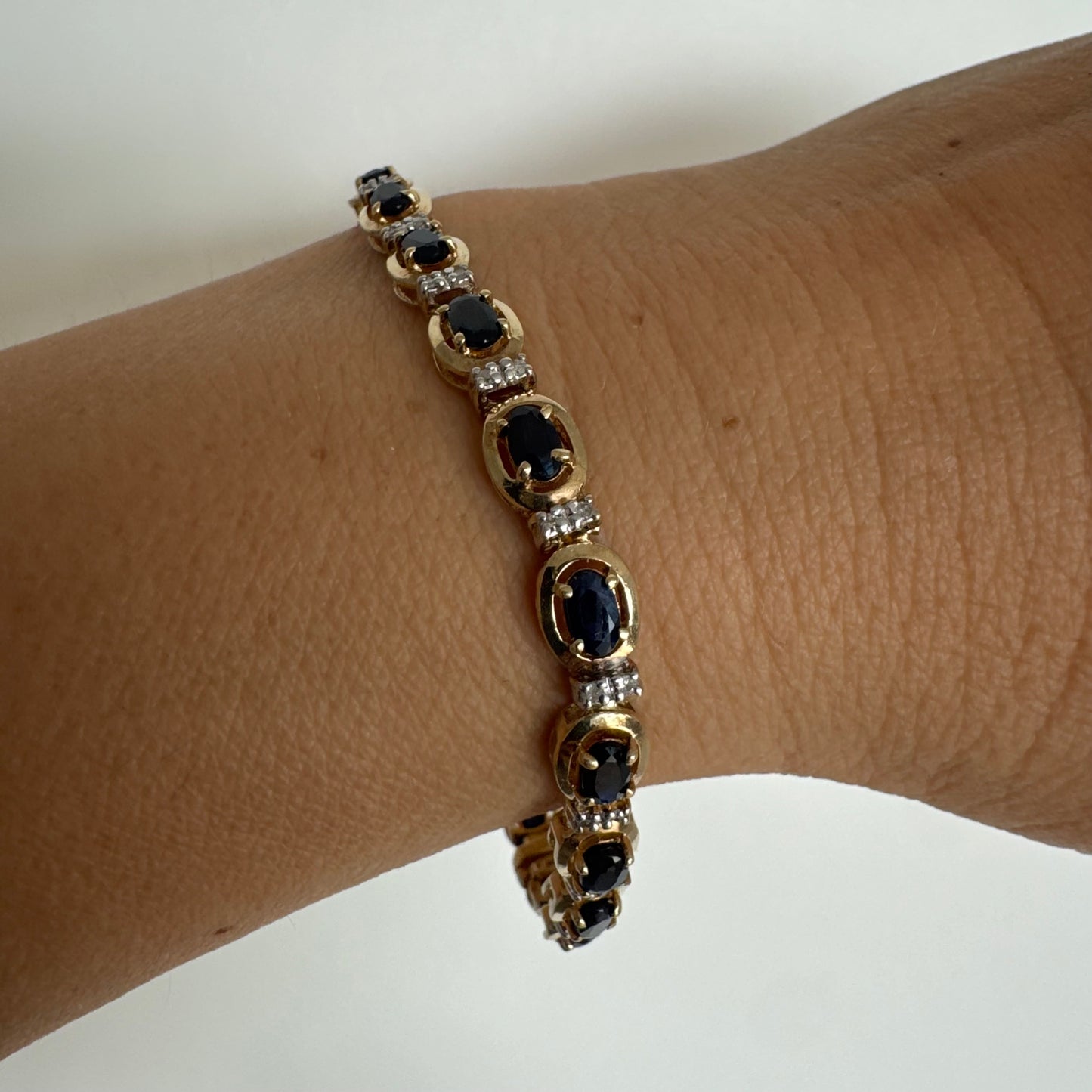 צמיד זהב צהוב 10 קראט בעיצוב קלאסי ועשיר, משובץ אבני ספיר אובליות בגוון כחול עמוק וביניהן שיבוצי יהלומים לבנים עדינים.