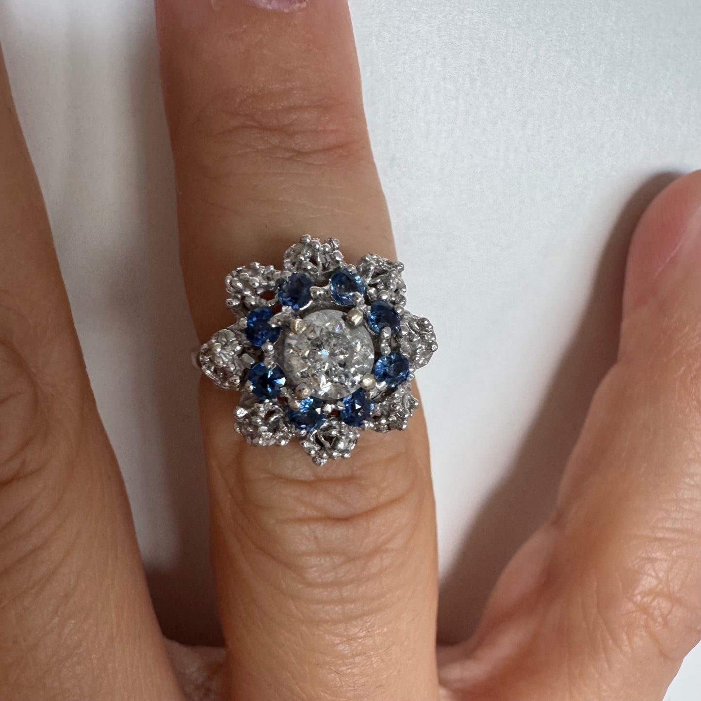 18K gold ring featuring a large round Diamond at the center, surrounded by a floral halo of purple -blue Tanzanite and & Diamonds.