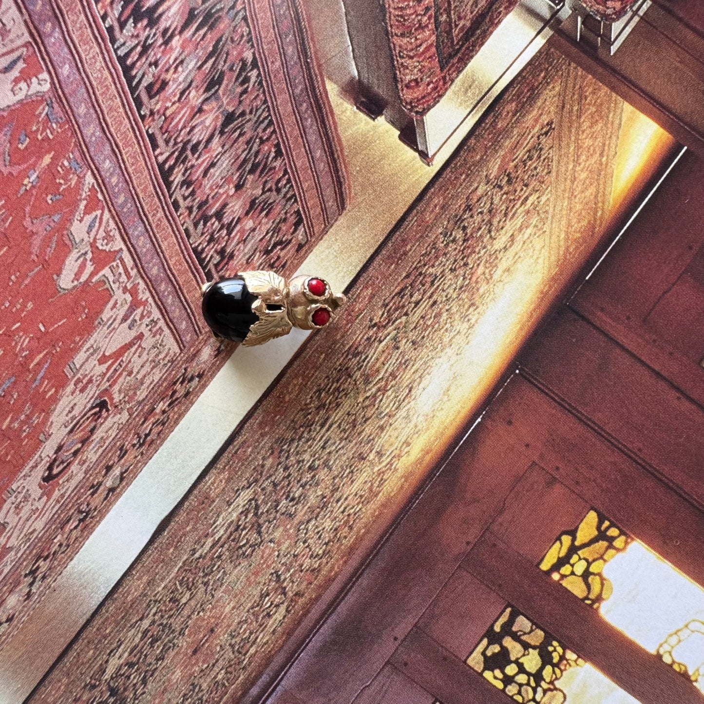 תליון בצורת חיפושית מזהב 14 קראט, עם עיניים אדומות מאבן קורל בחיתוך קבושון וגוף מאבן אוניקס שחורה מבריקה.