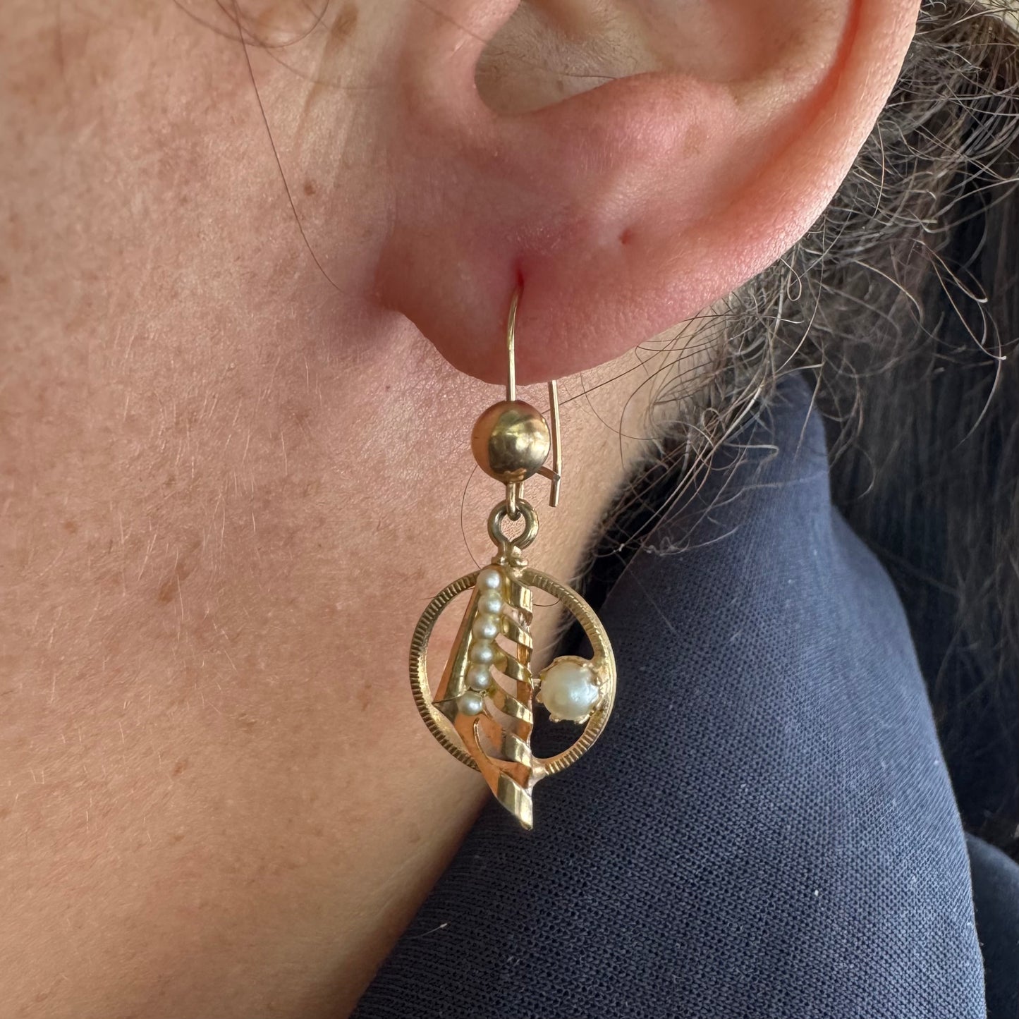 עגילי זהב 10 קראט, בעיצוב עדין עם אלמנט ספירלי ושילוב פנינים קטנות בגוון לבן-קרם. 