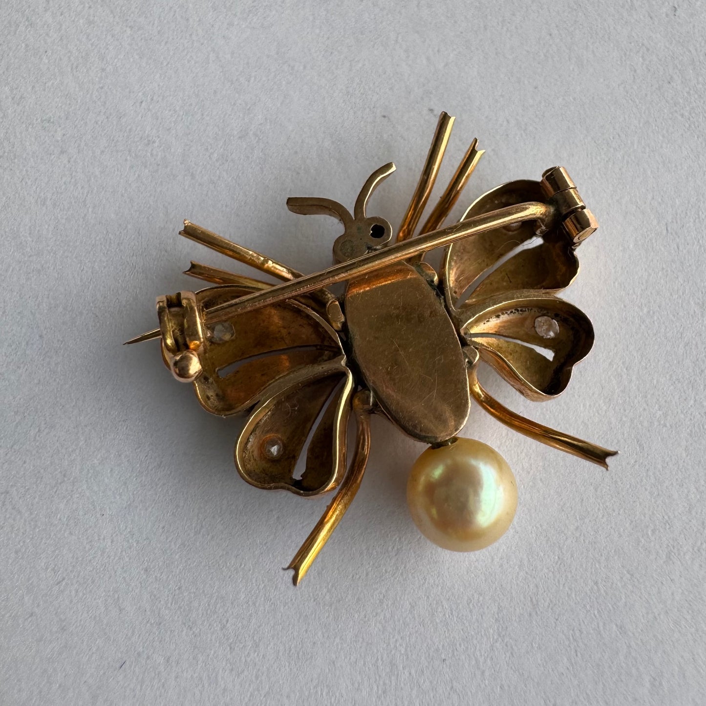 סיכת חרק ייחודית עשויה זהב 14 קראט משובצת יהלומים בעבודת פיליגרן עדינה בכנפיים, אבני רובי אדומות בעיניים ופנינה טבעית בגוון שמפניה.