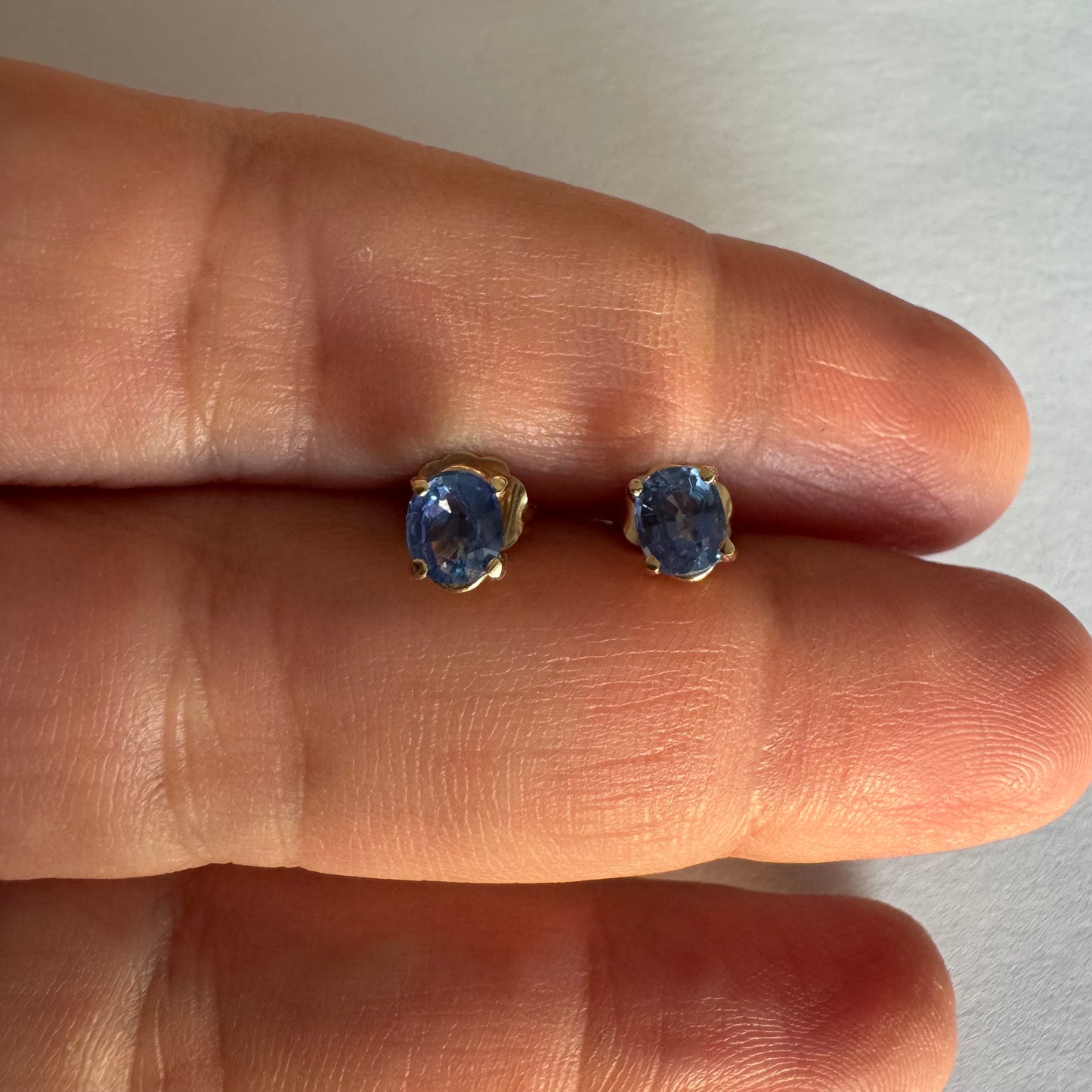 עגילי זהב 14 קראט קטנים צמודים לאוזן משובצים אבני טנזנייט בחיתוך אובלי, בגוון כחול־סגלגל עמוק ומעודן.