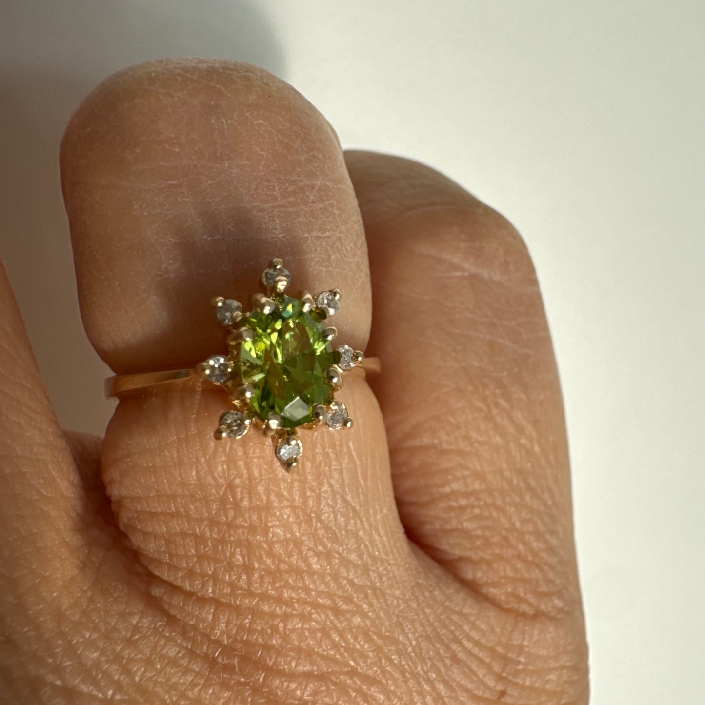 טבעת זהב 14 קראט משובצת אבן פרידוט ירוקה בחיתוך אובלי, מוקפת יהלומים היוצרים הילה עדינה מסביבה.