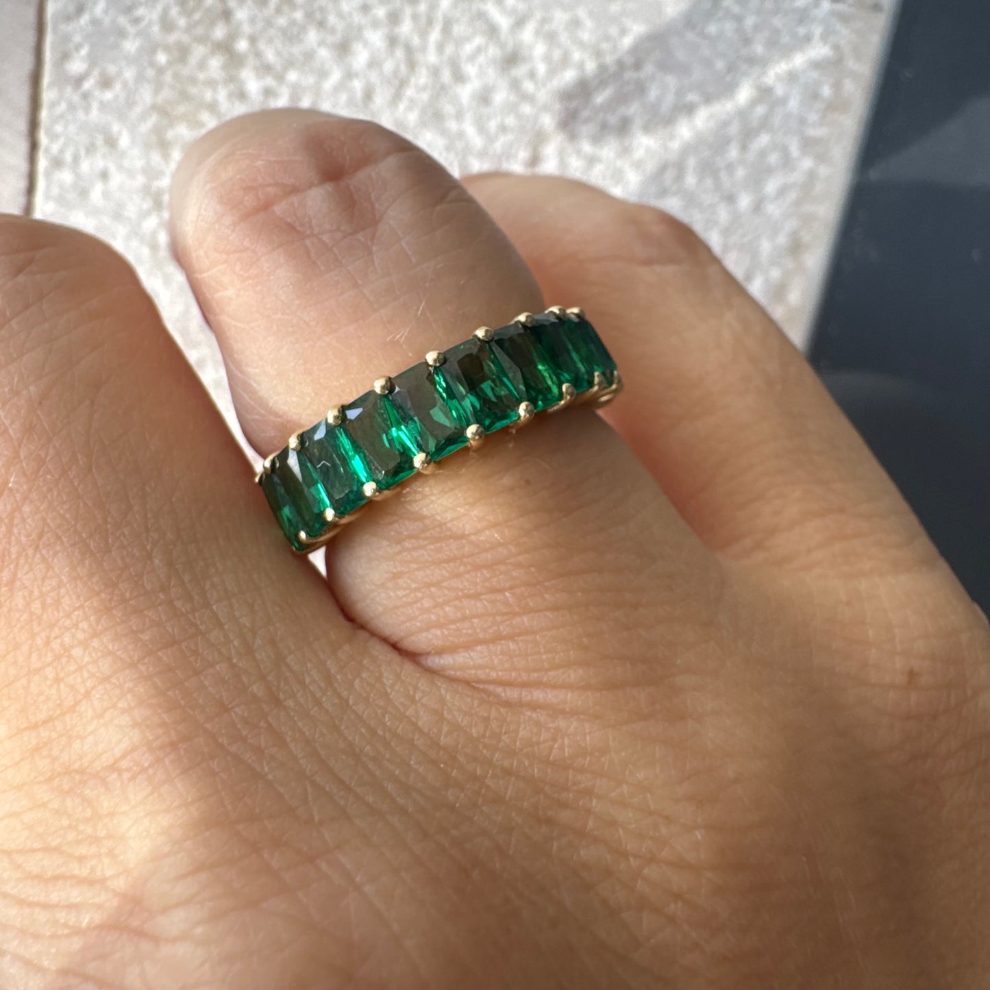 טבעת זהב צהוב 14 קראט משובצת אבנים ירוקות בחיתוך אמרלד, בעיצוב חצי איטרניטי.