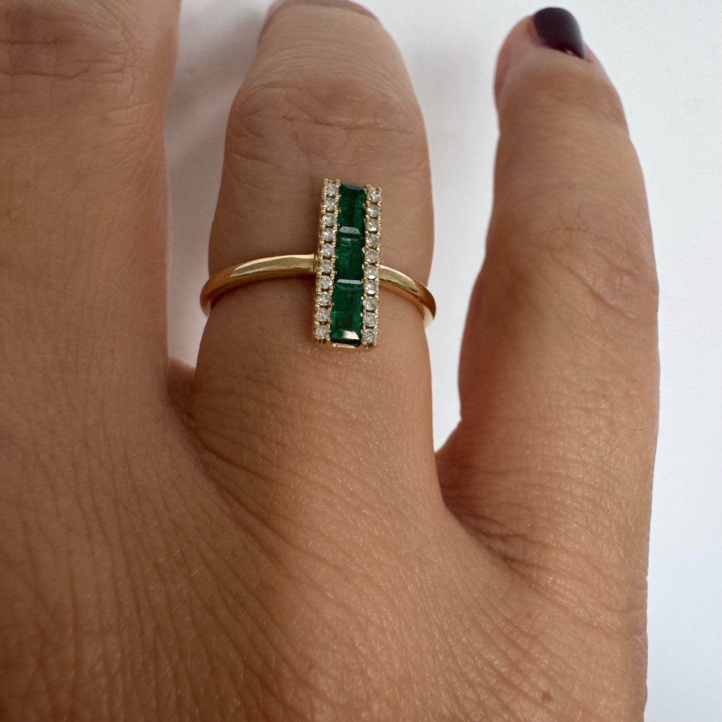 טבעת זהב 14 קראט משובצת אבני אמרלד בחיתוך באגט, מוקפות בשתי שורות של יהלומים נוצצים .