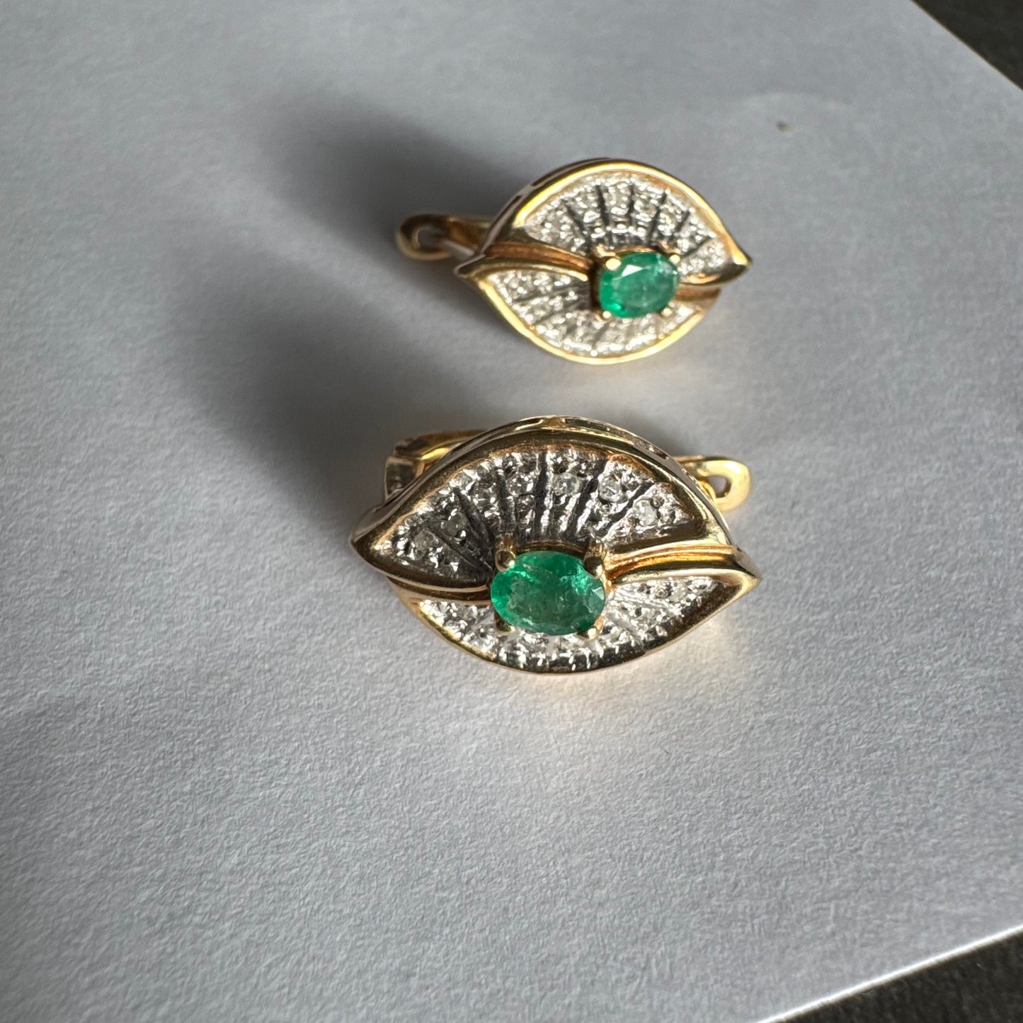 עגילים צמודים לאוזן, זהב צהוב 14 קראט, משובצים אמרלד במרכז, וסביבן פיתוחים משובצים יהלומים, שמעניקים מראה של ניצוץ רך ואלגנטי