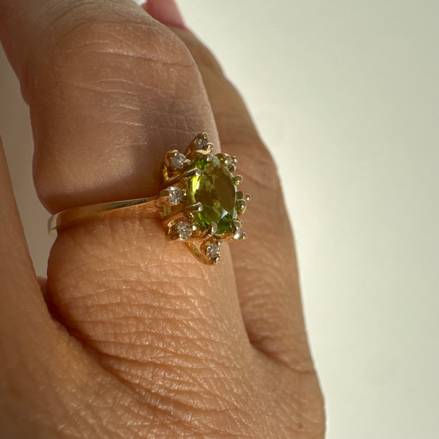 טבעת זהב 14 קראט משובצת אבן פרידוט ירוקה בחיתוך אובלי, מוקפת יהלומים היוצרים הילה עדינה מסביבה.