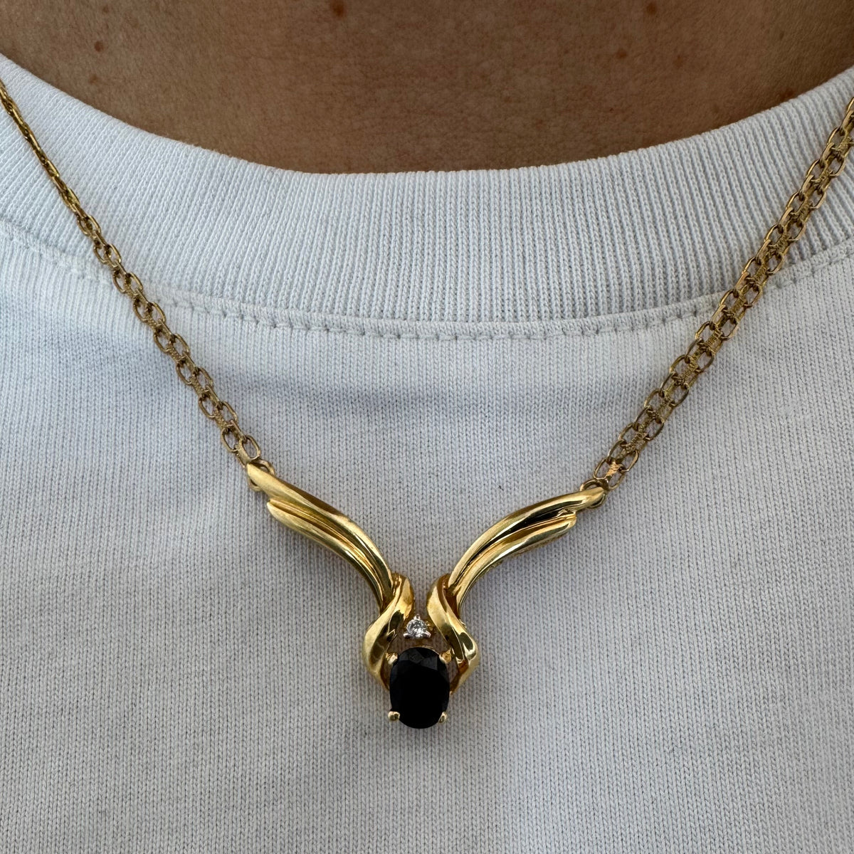14K gold necklace featuring a flowing pendant design, set with a dark blue center Sapphire and a small Diamond above.