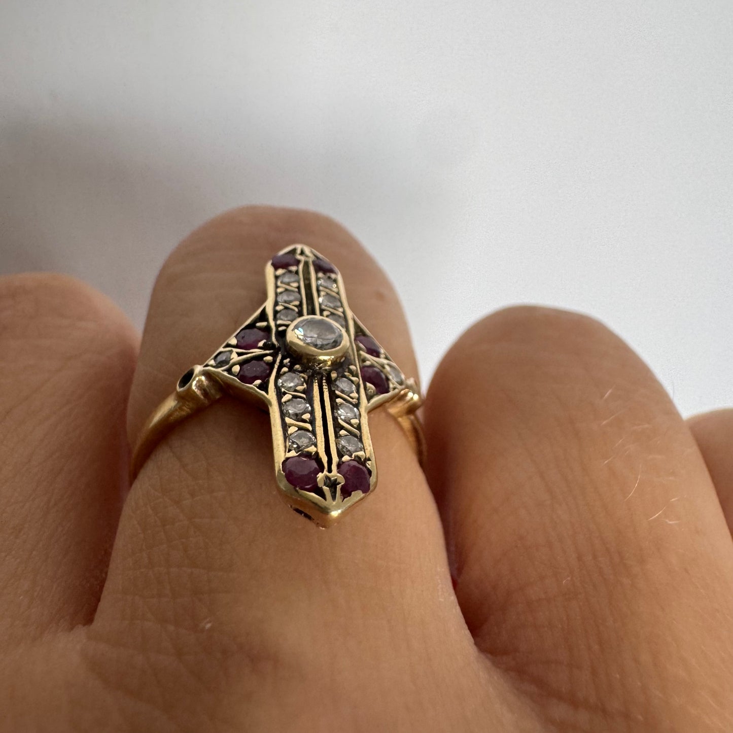 18K gold ring featuring a striking geometric design, set with a central Diamond surrounded by sparkling Diamonds and rich red Rubies.